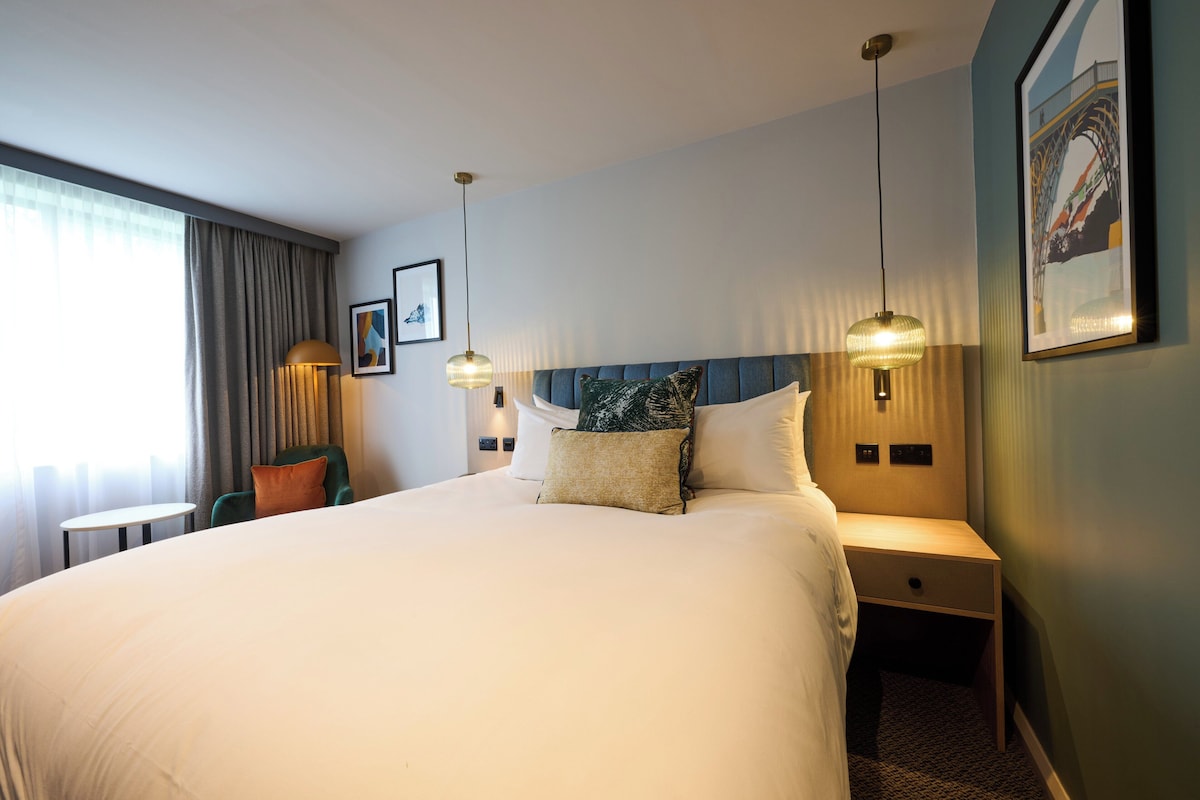 A hotel room with a large bed, bedside tables, a chair, and a view of the outdoors.