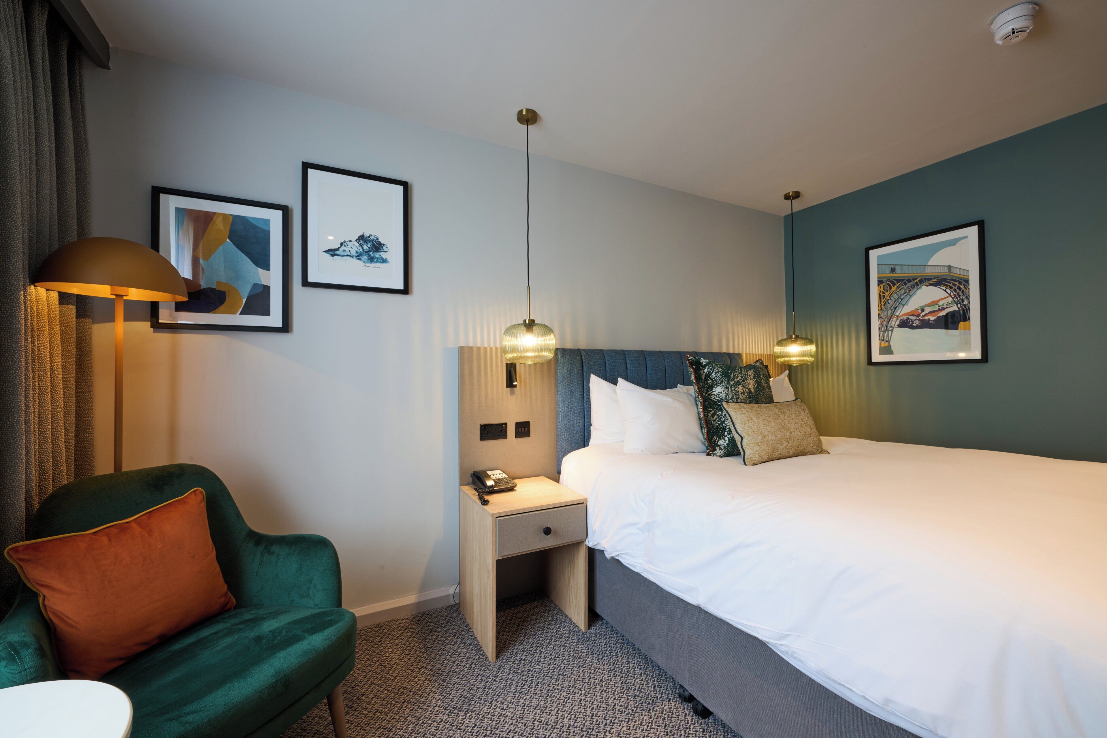 A hotel room with a bed, a desk, a chair, and two wall-mounted lamps.