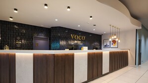 A reception desk with a dark tiled wall and a sign that reads 'VOCO BEING'. - voco Telford - Ironbridge by IHG (Telford)