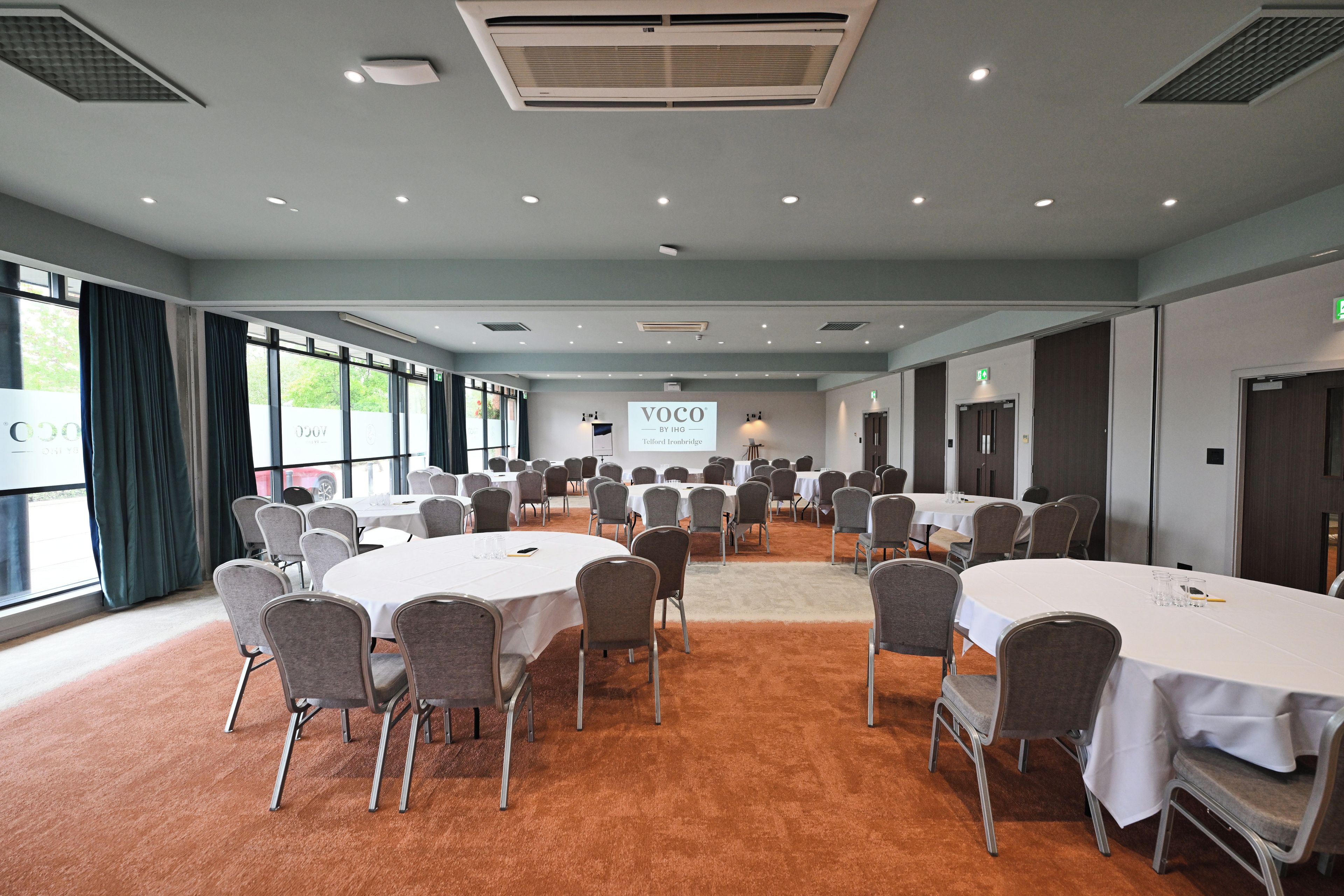 A conference room with round tables, chairs, and a large projection screen.