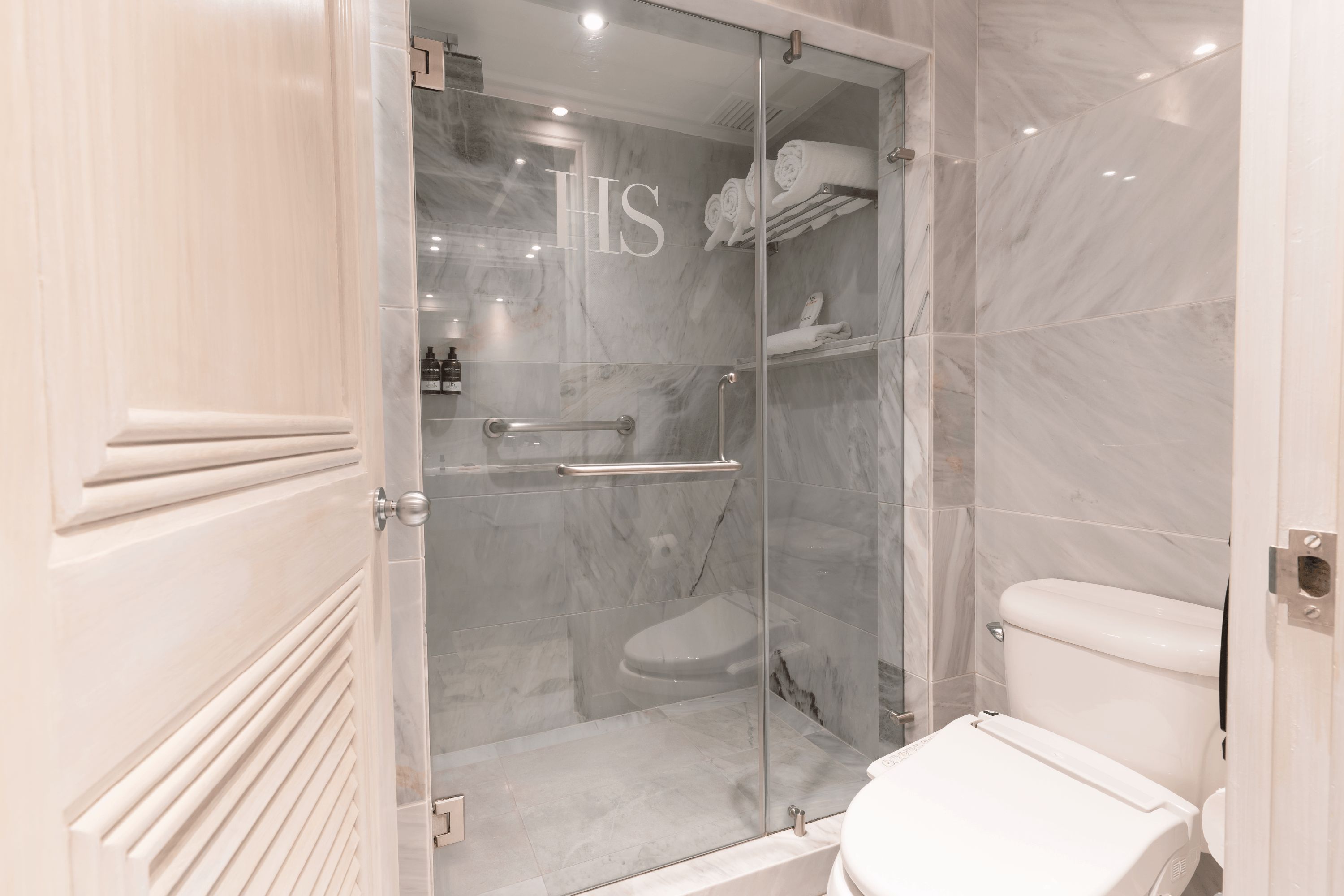 A modern bathroom with a glass-enclosed shower, a toilet, and marble flooring.