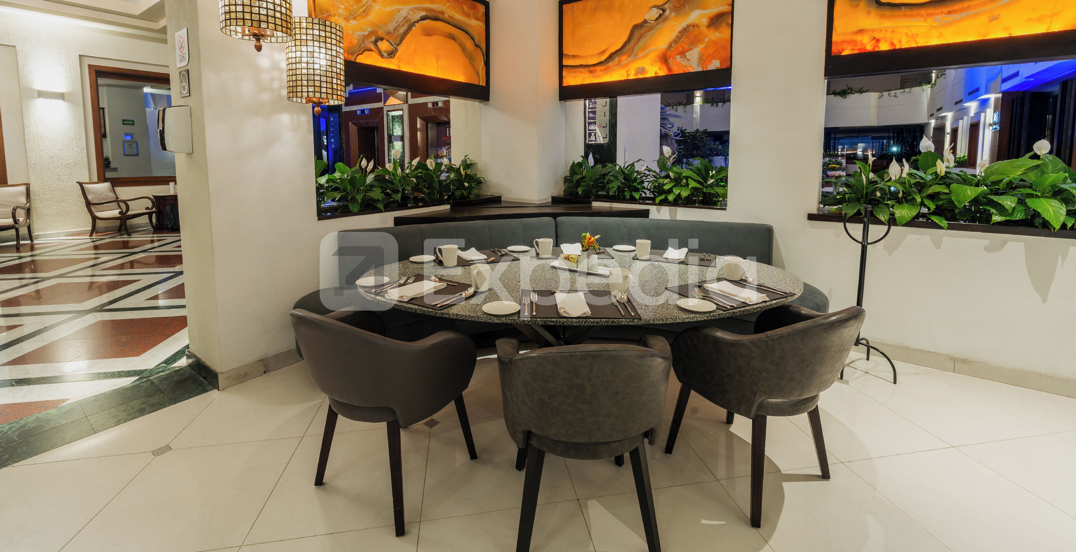Uma mesa de jantar redonda com cadeiras, piso de azulejos e uma parede com um grande quadro abstrato.