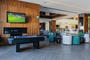 A modern lounge area with a pool table, comfortable seating, a television displaying a sports event, and a visible exit sign. - HS HOTSSON Hotel Leon (León)