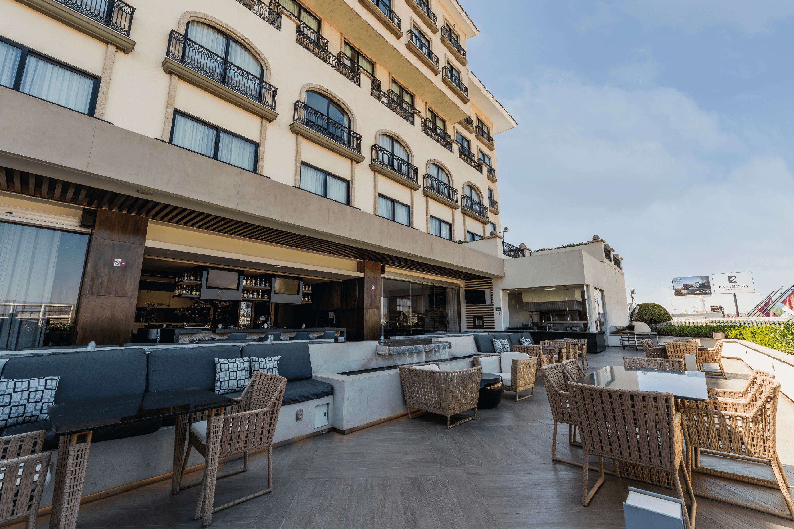 A rooftop bar with outdoor seating, a bar area, and a view of the building's facade.