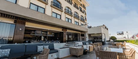 A rooftop bar with outdoor seating, a bar area, and a view of the building's facade.