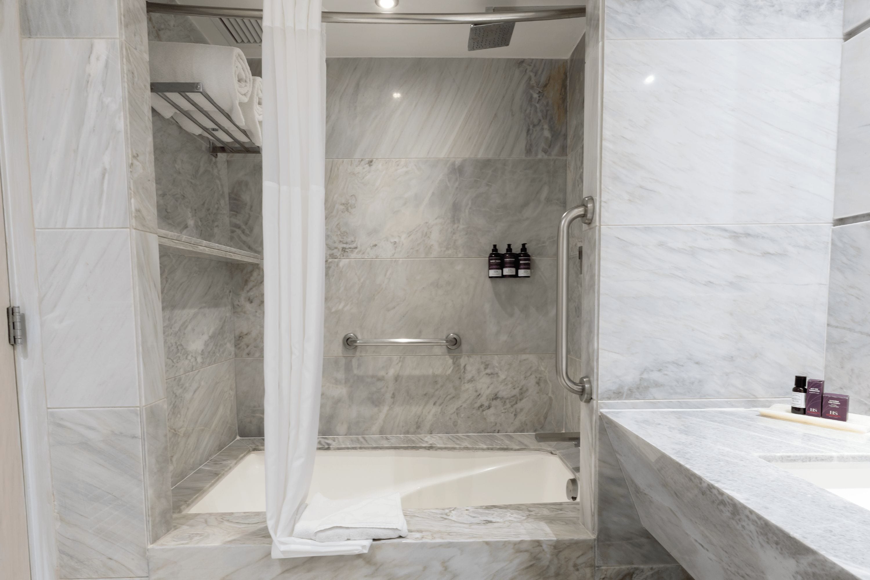 A modern bathroom with a walk-in shower, marble tiles, and a bathtub.