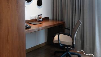 Una habitación de hotel con un escritorio de madera, una silla, un teléfono y un enchufe en la pared.