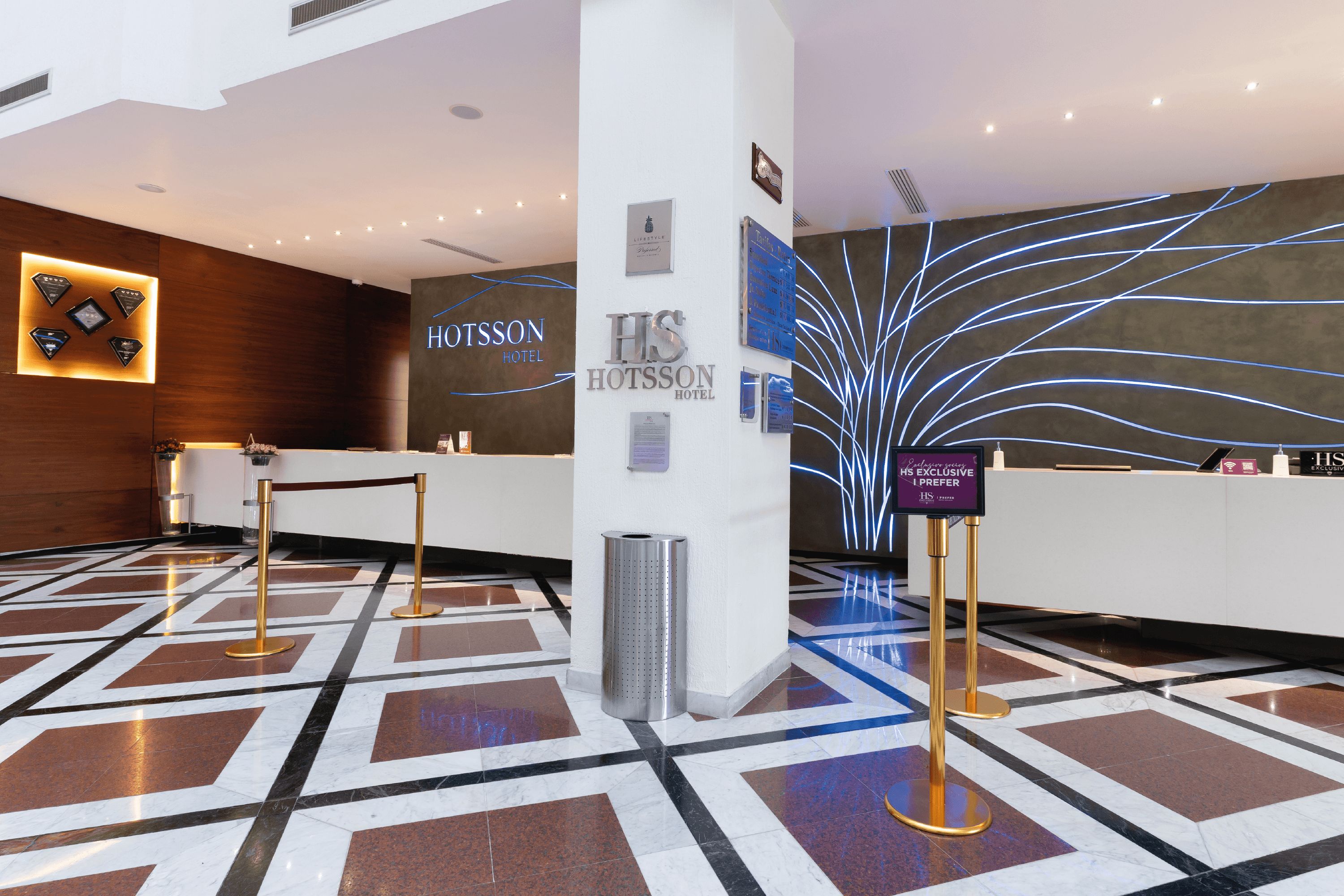 A hotel reception area with a modern design, including a reception desk, a wall-mounted sign, and a decorative light installation.
