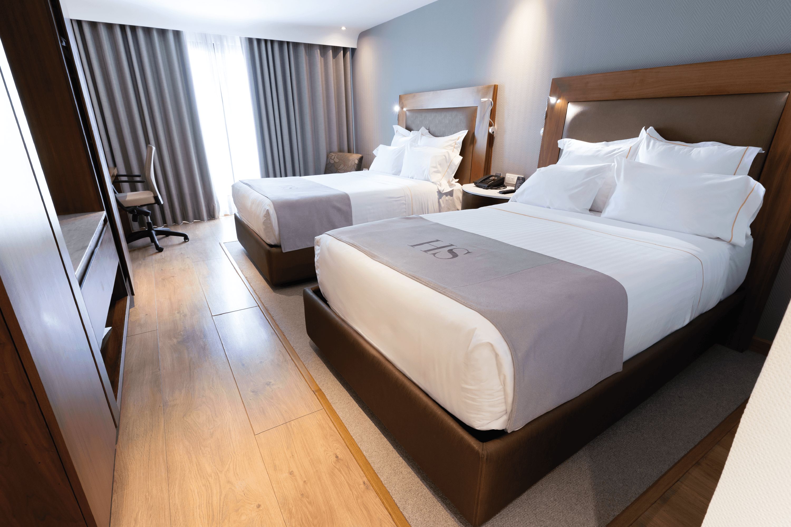 A hotel room with two beds, a desk, and a chair.
