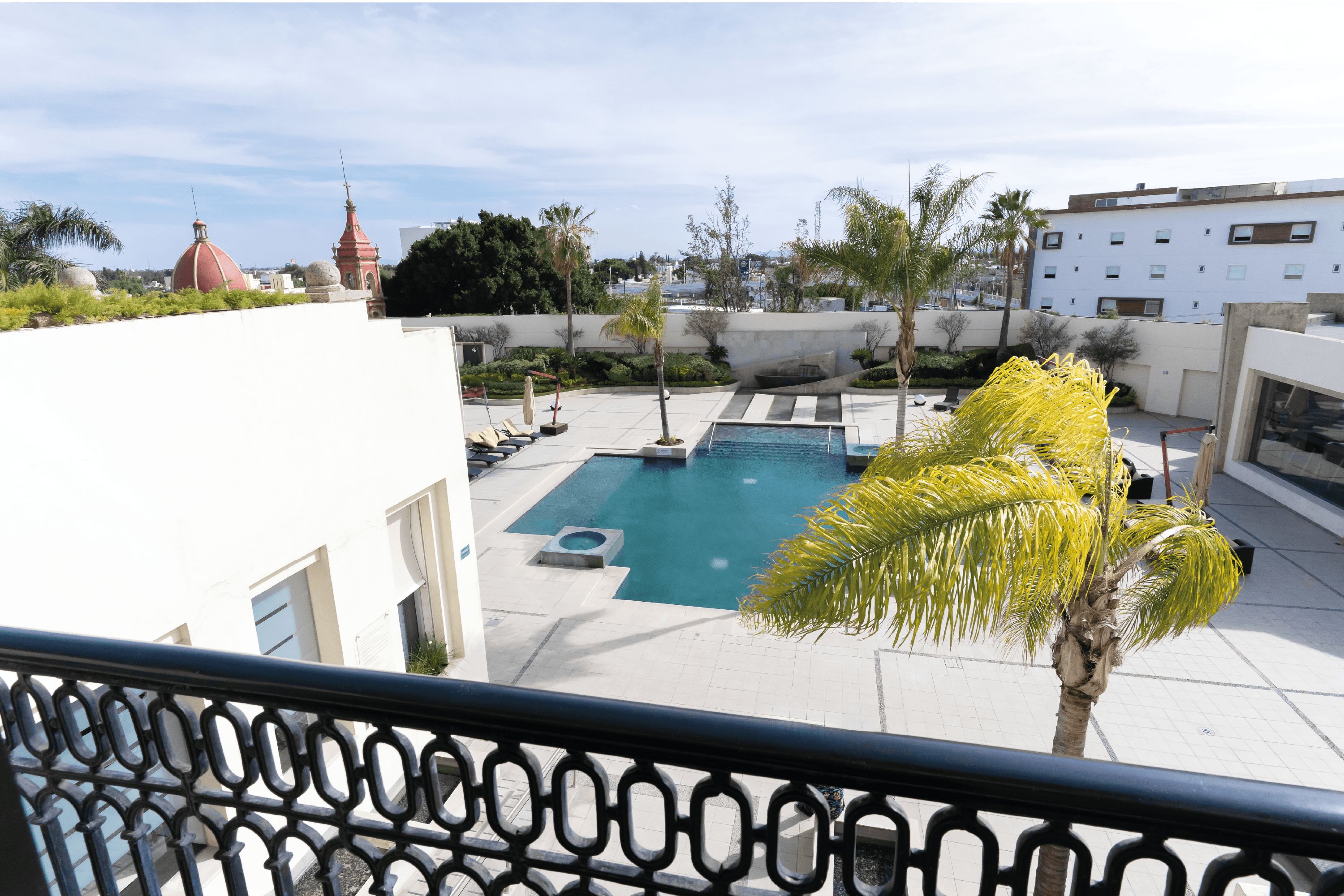 A rooftop swimming pool with a view of the cityscape, surrounded by palm trees and modern buildings.