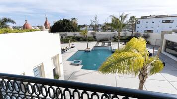A rooftop swimming pool with a view of the cityscape, surrounded by palm trees and modern buildings.