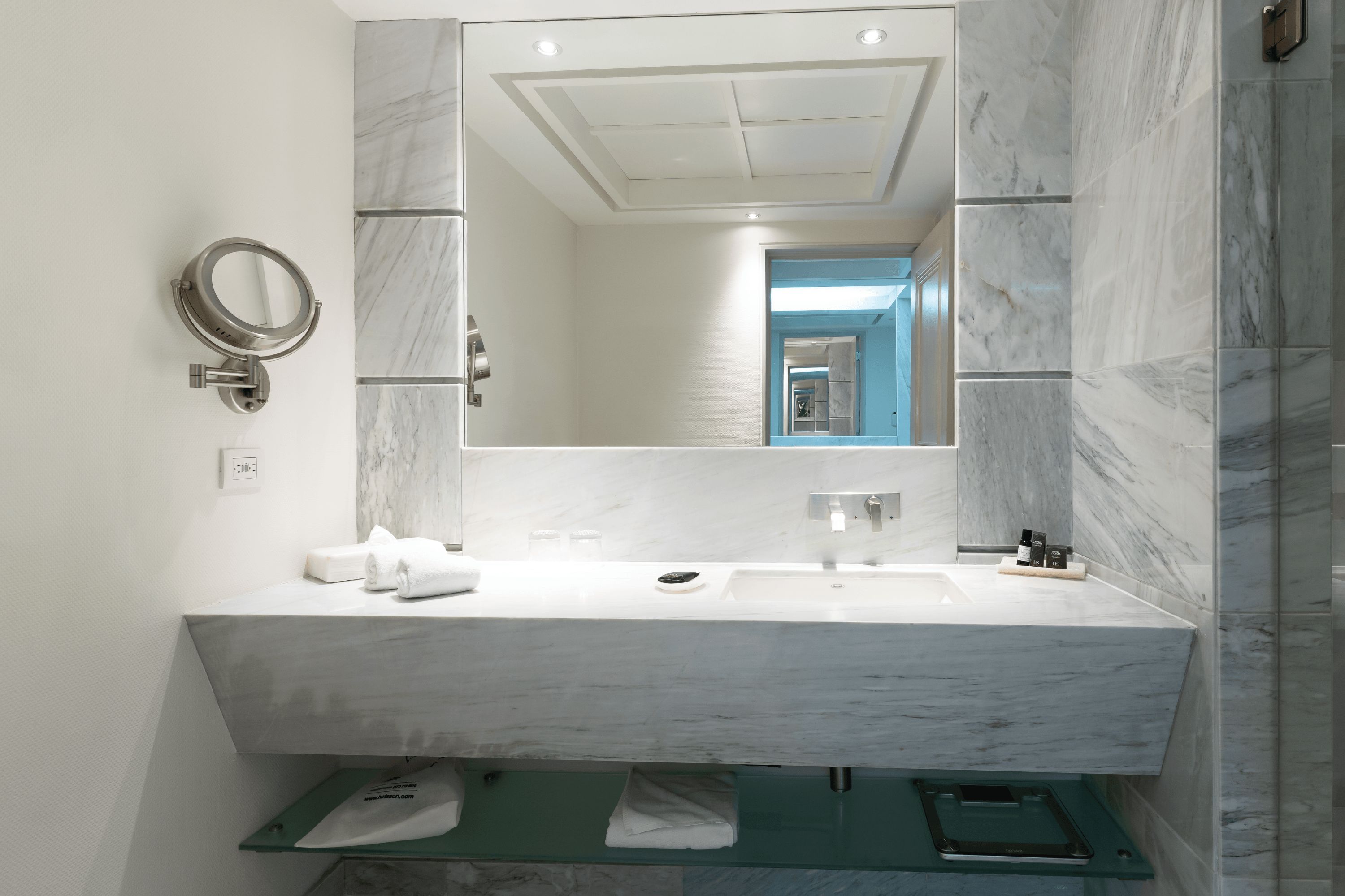 A modern bathroom with a marble sink, a large mirror, and a glass shower enclosure.