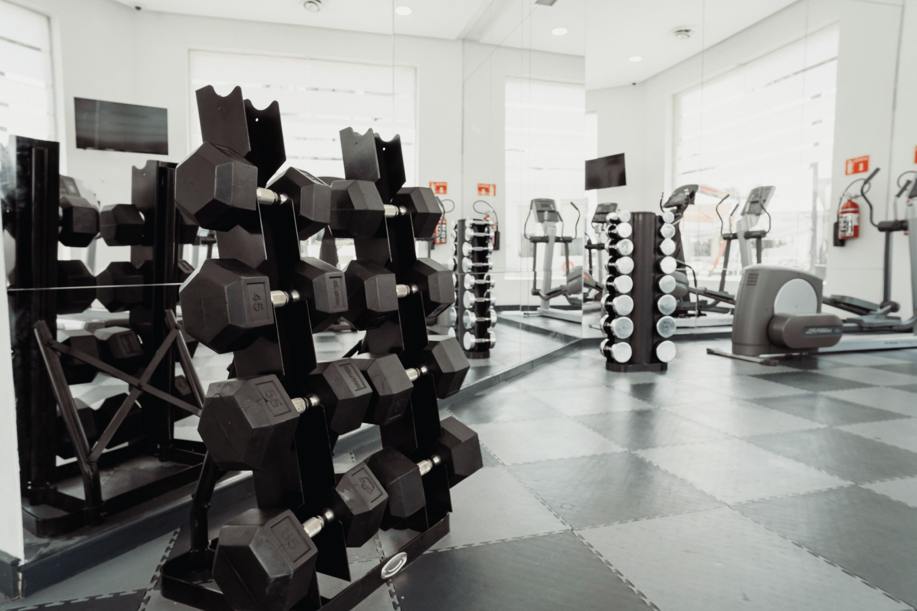 Ein Fitnessstudio mit unterschiedlichen Trainingsgeräten, darunter Hanteln und Laufbänder.