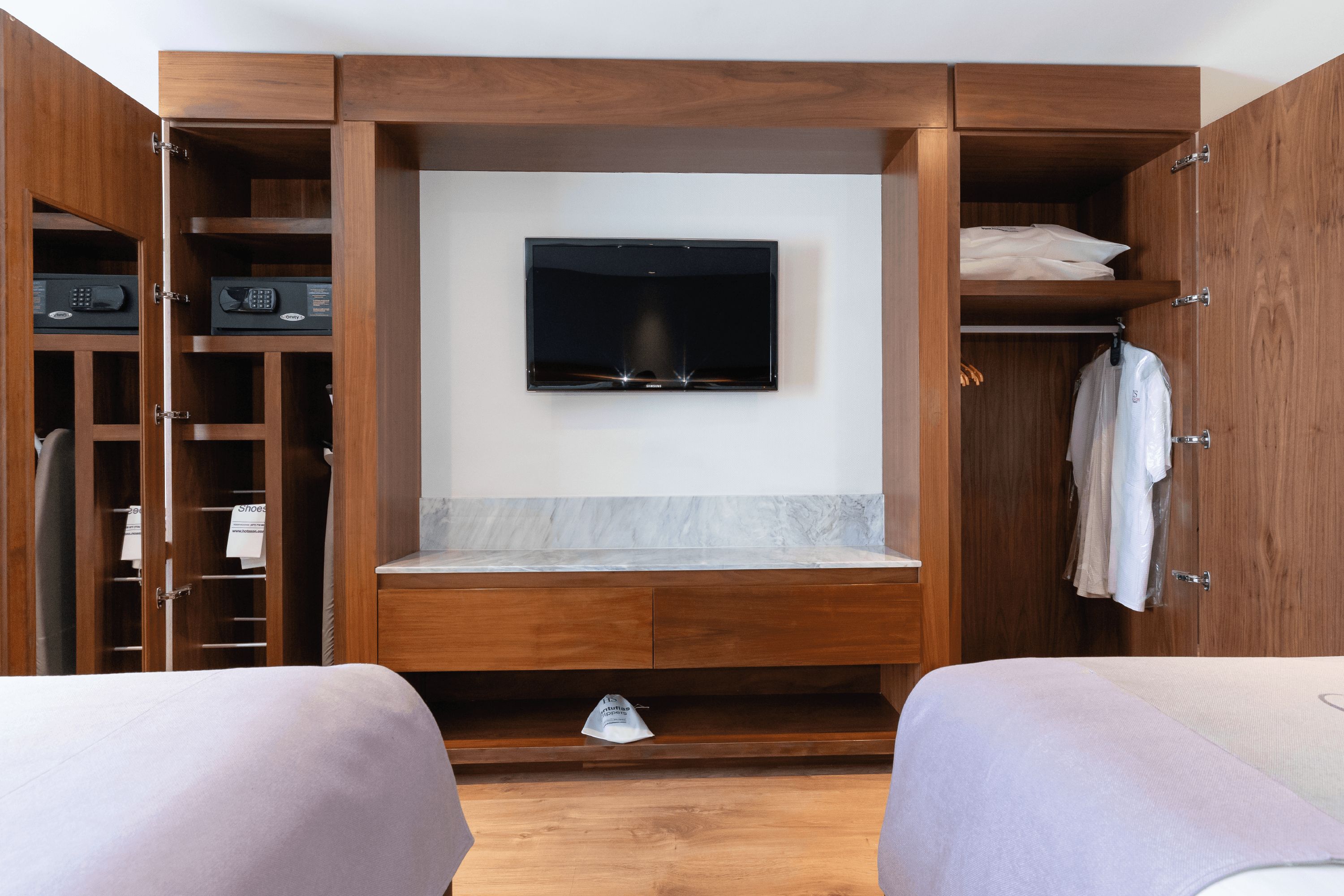 A hotel room with a built-in TV, wooden wardrobe, and a marble countertop.
