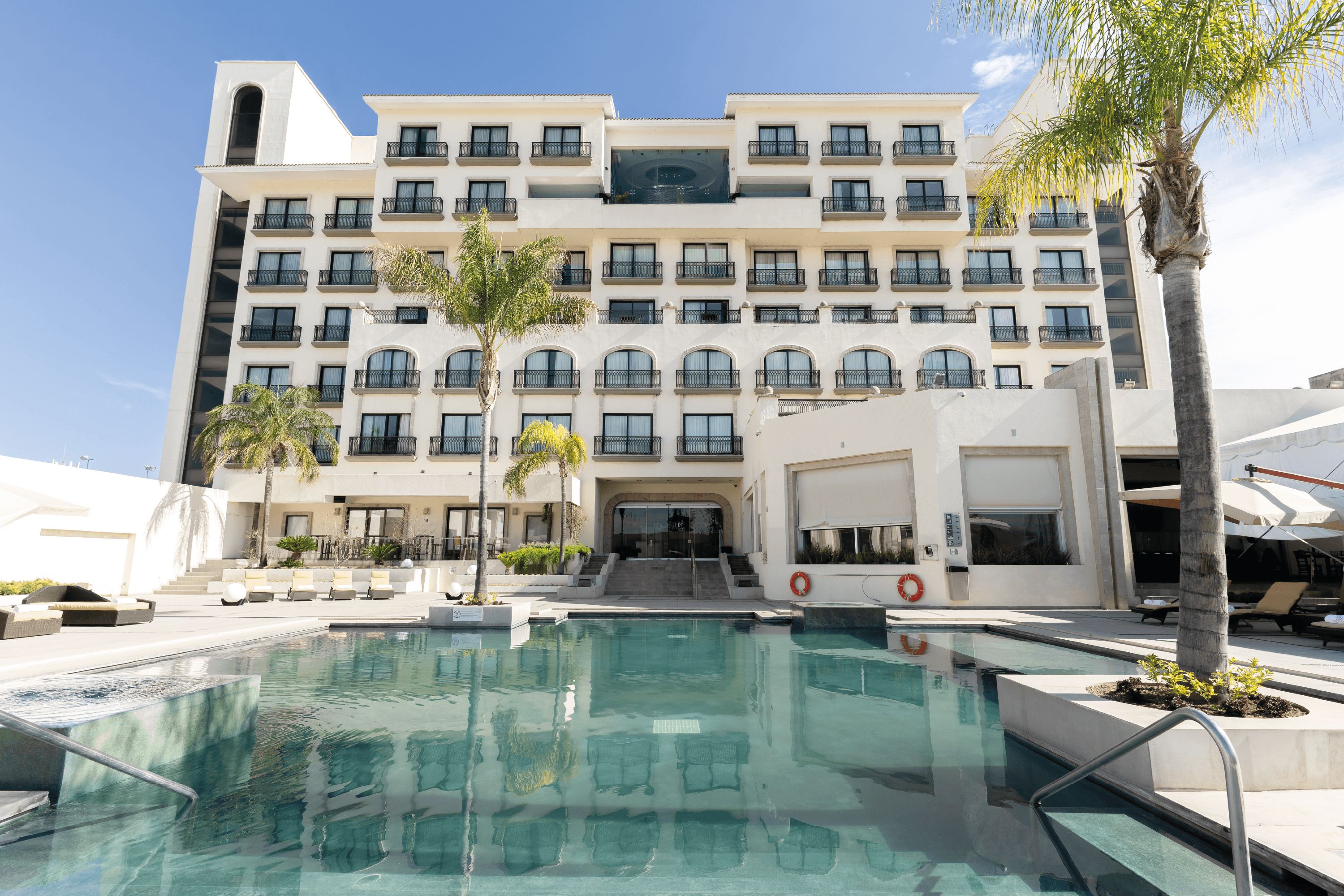 A hotel with a swimming pool, multiple balconies, and a clear sky.