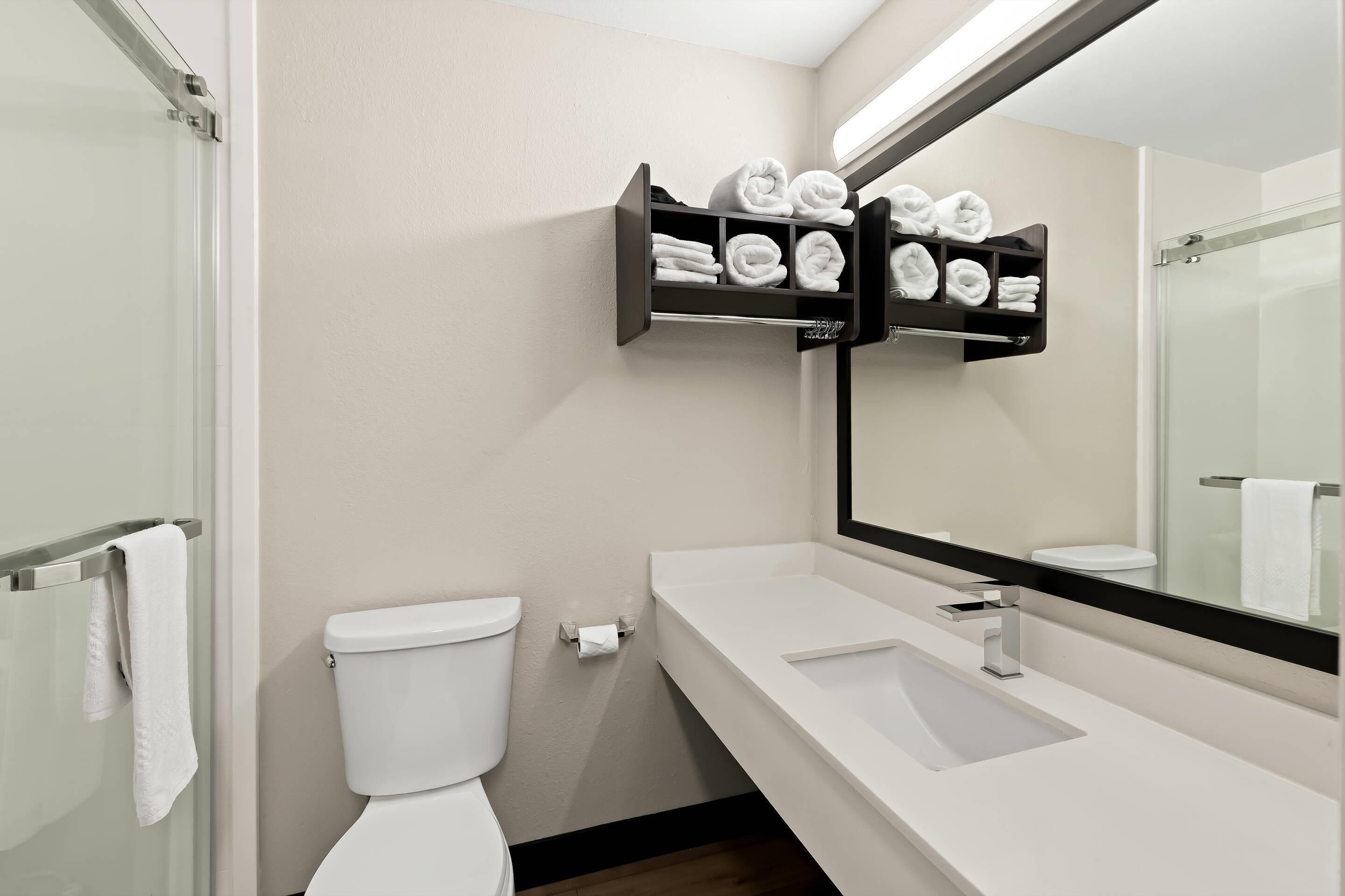 A modern bathroom with a white sink, a toilet, a glass shower enclosure, and a towel rack with neatly folded towels.
