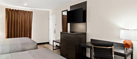 Una habitación de hotel con dos camas, un escritorio con silla, un aparador, un televisor montado en la pared y una lámpara sobre el escritorio.