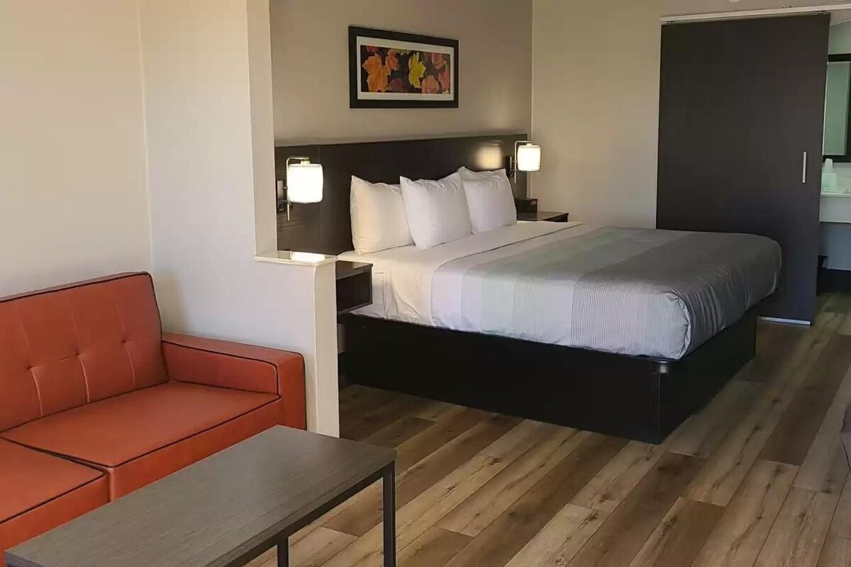 A hotel room with a bed, a nightstand, a red sofa, and a small table.