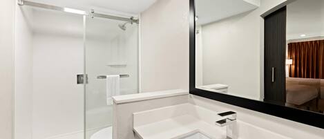 Een moderne badkamer met een douchecabine van glas, een witte wastafel met een zwarte kraan en een grote spiegel.