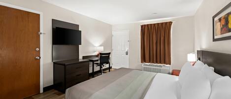 Quarto de hotel com cama, escrivaninha, cadeira, televisão e janela com cortinas.