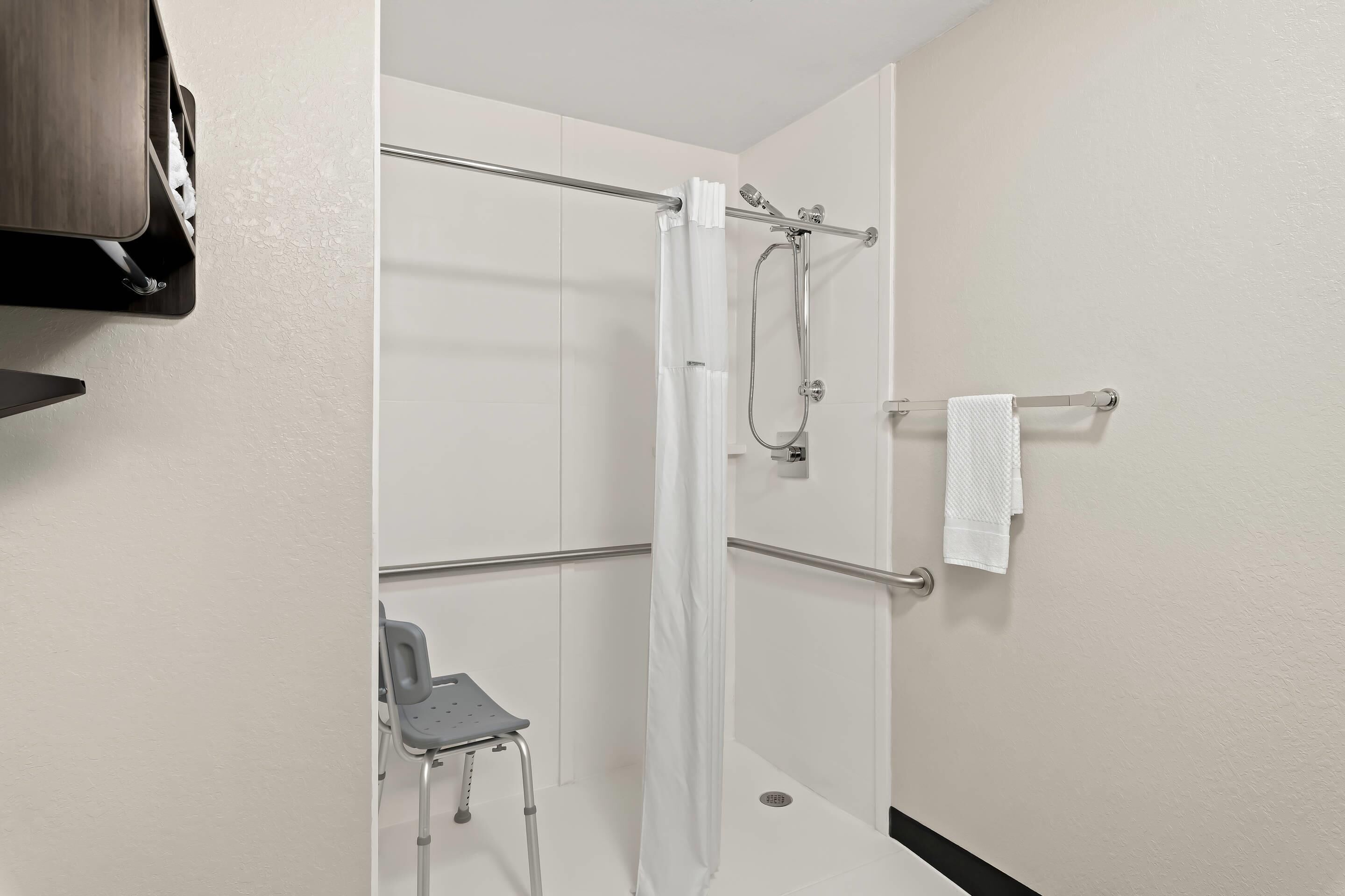 A shower area with a glass door, a towel rack, and a wheelchair-accessible bench.