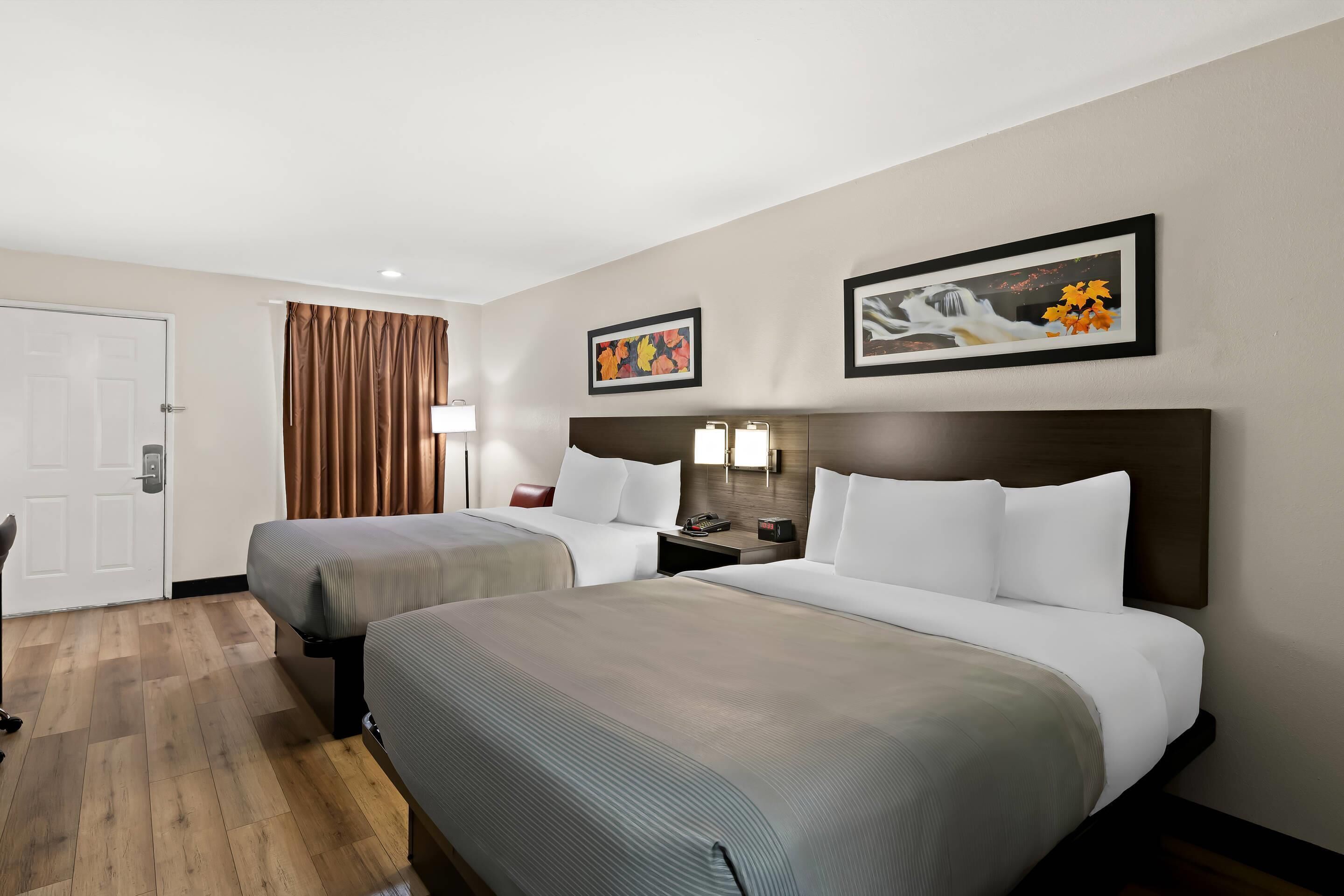 Habitación de hotel con dos camas, una puerta, una cortina y dos lámparas fijadas a la pared.