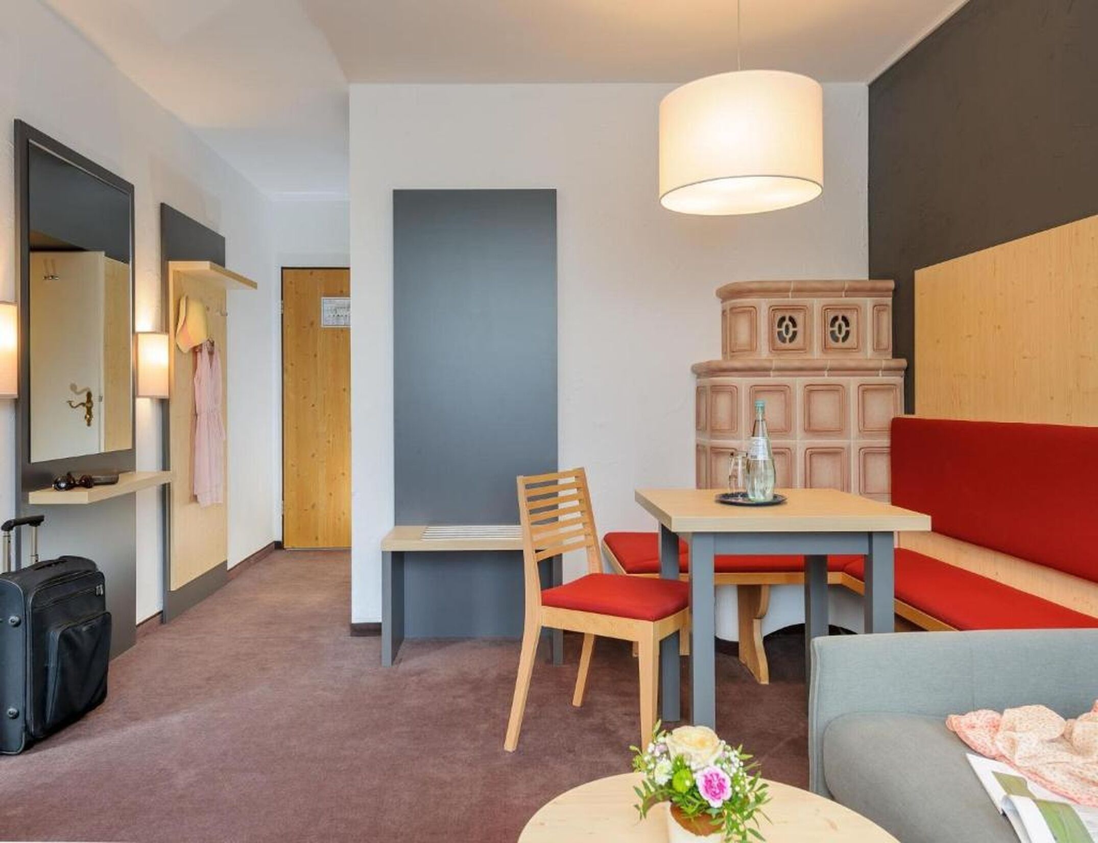Een hotelkamer met een bed, bureau, stoel, tafel, bank en een lamp, plus een koffer.