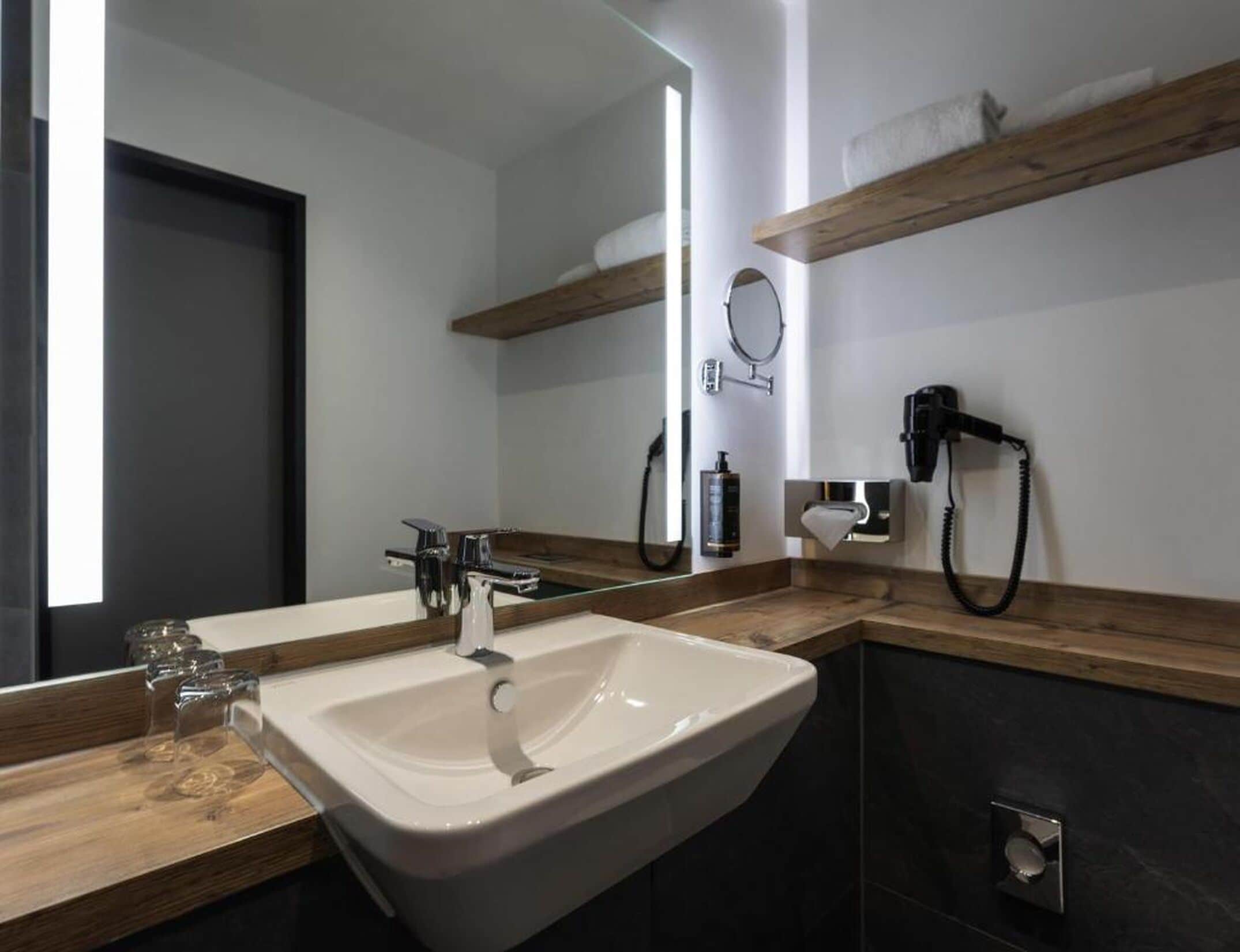 A modern bathroom with a large mirror, a sink, and a hairdryer mounted on the wall.