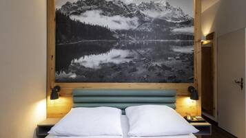Un letto con biancheria bianca, una testiera in legno e un'ampia immagine incorniciata di un paesaggio montano sopra di esso.