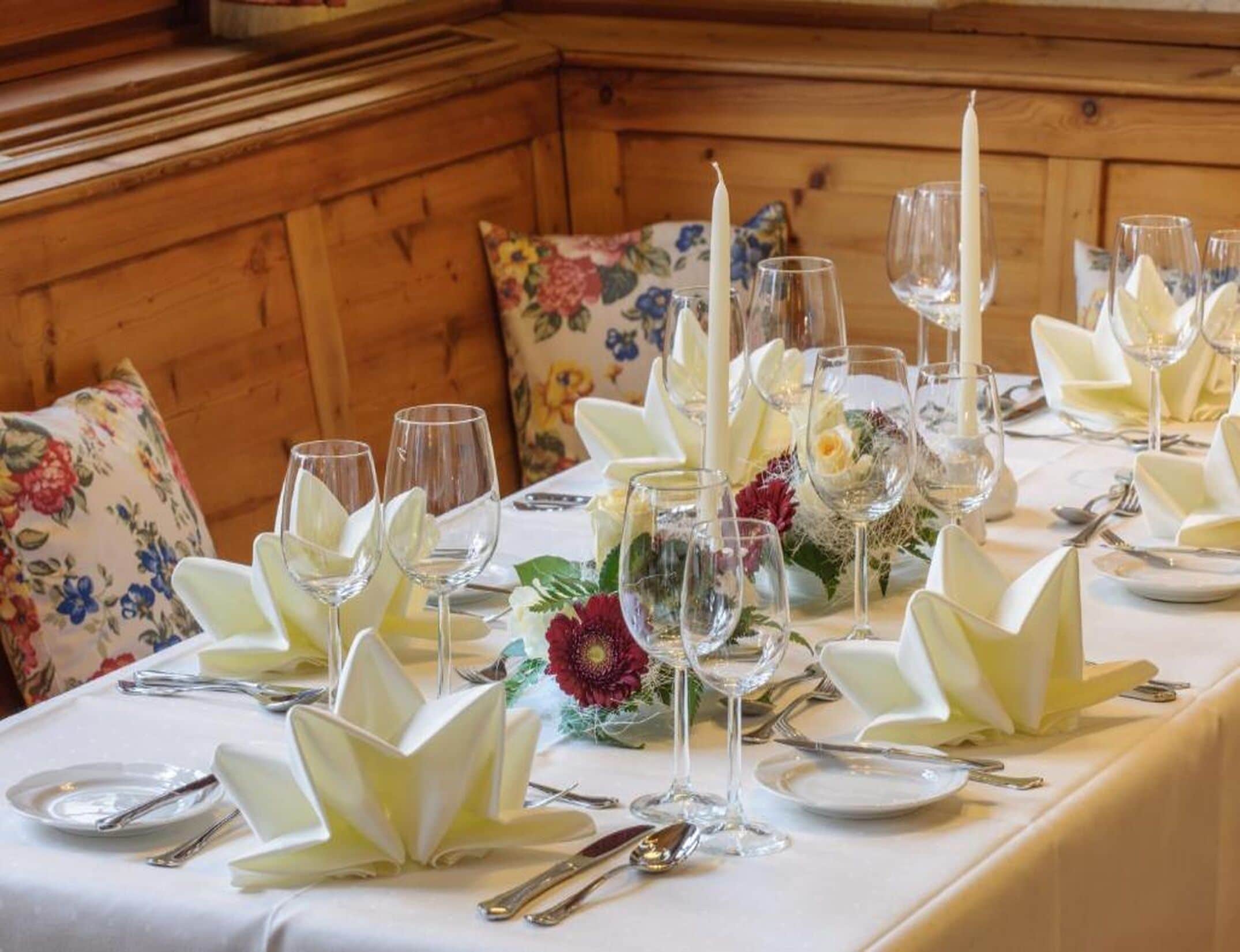 A table set for a formal dinner with white tablecloths, glassware, and floral centerpieces.