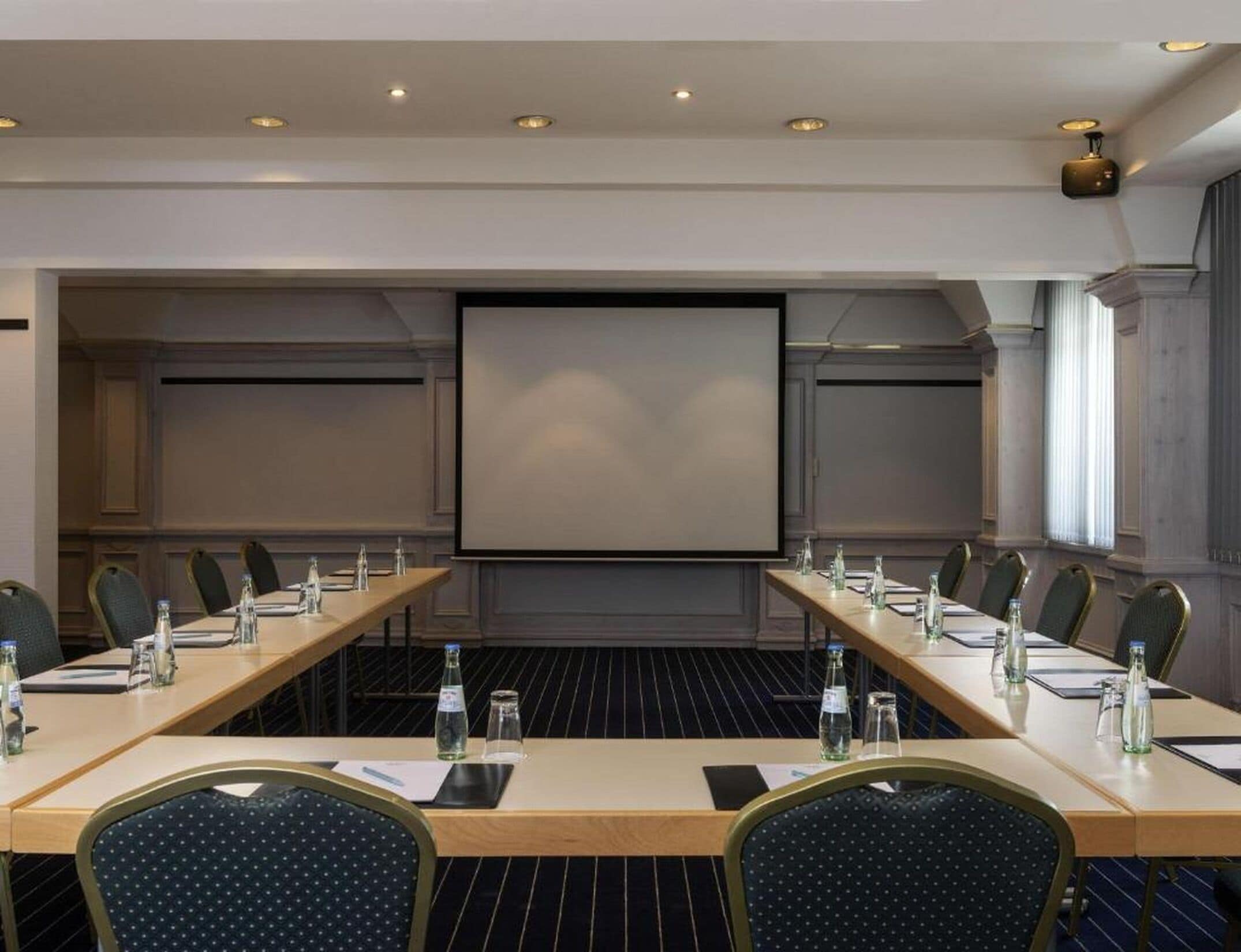 A conference room with a long table, chairs, a projector screen, and a large window.