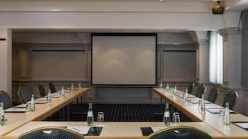 A conference room with a long table, chairs, a projector screen, and a large window.