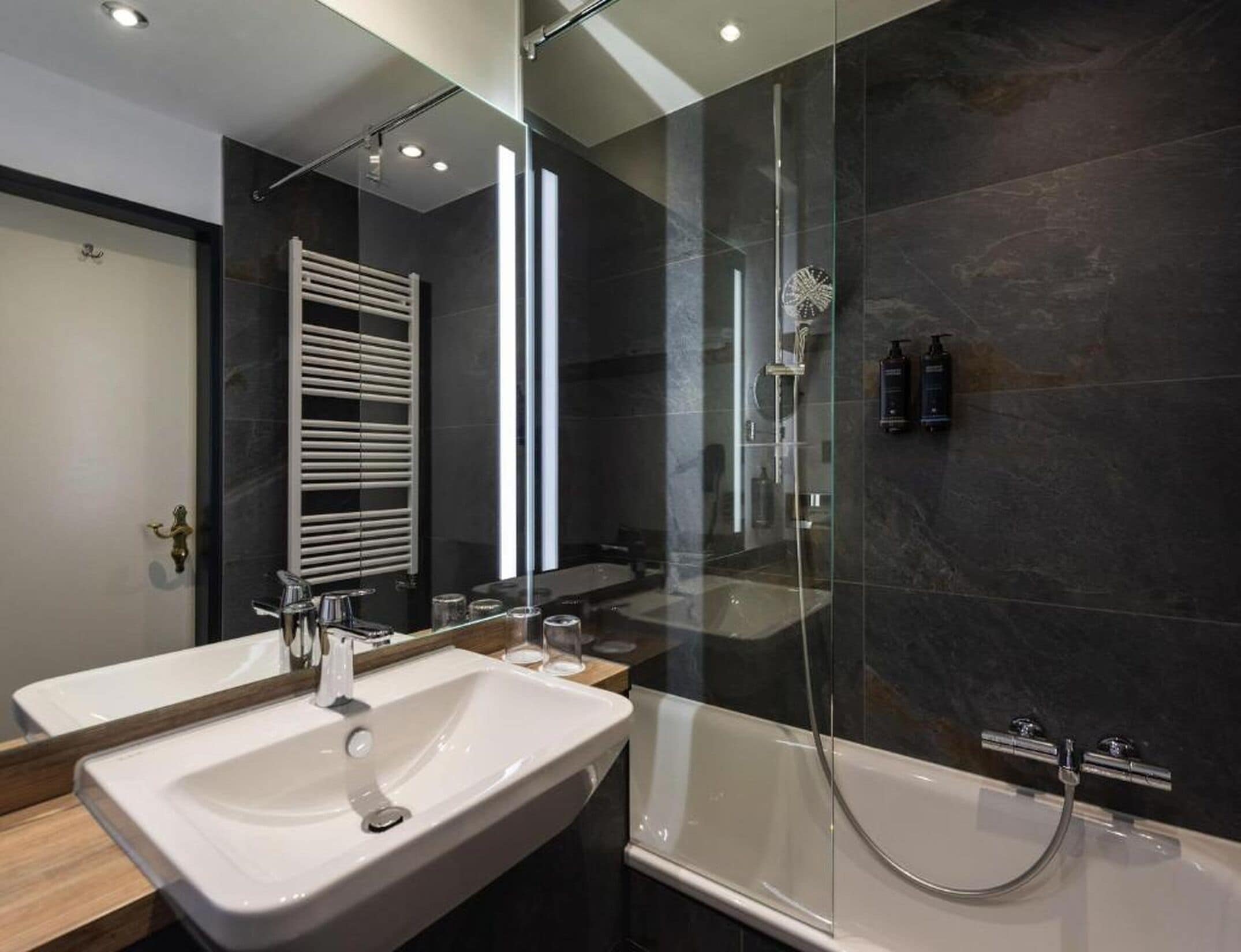 A modern bathroom with a double sink, a glass shower enclosure, and a towel rack.