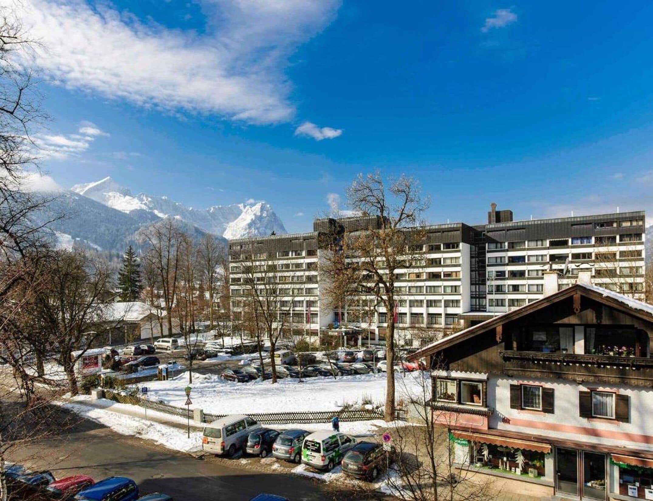 A hotel with multiple floors, a parking lot with several cars, and a mountain range in the background.