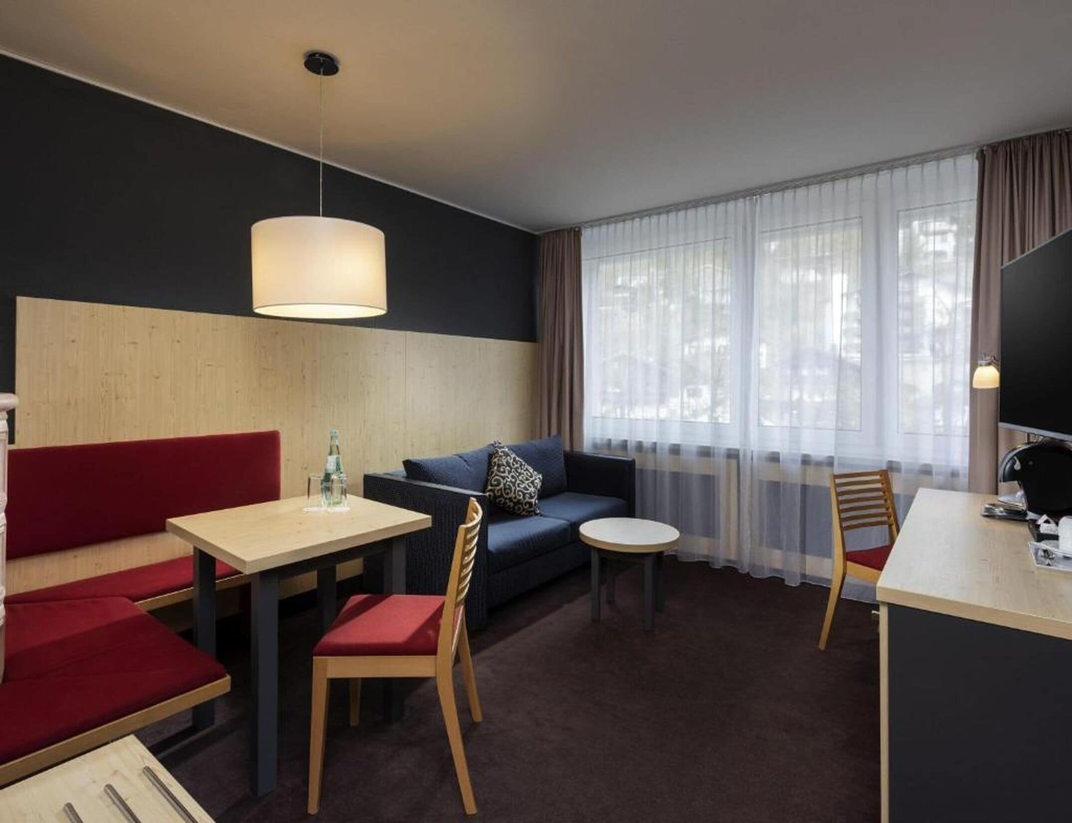 Habitación de hotel con sofá, una mesa de comedor, una mesita redonda y un televisor.