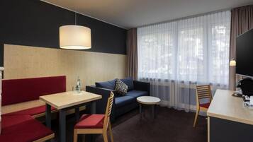 Habitación de hotel con sofá, una mesa de comedor, una mesita redonda y un televisor.