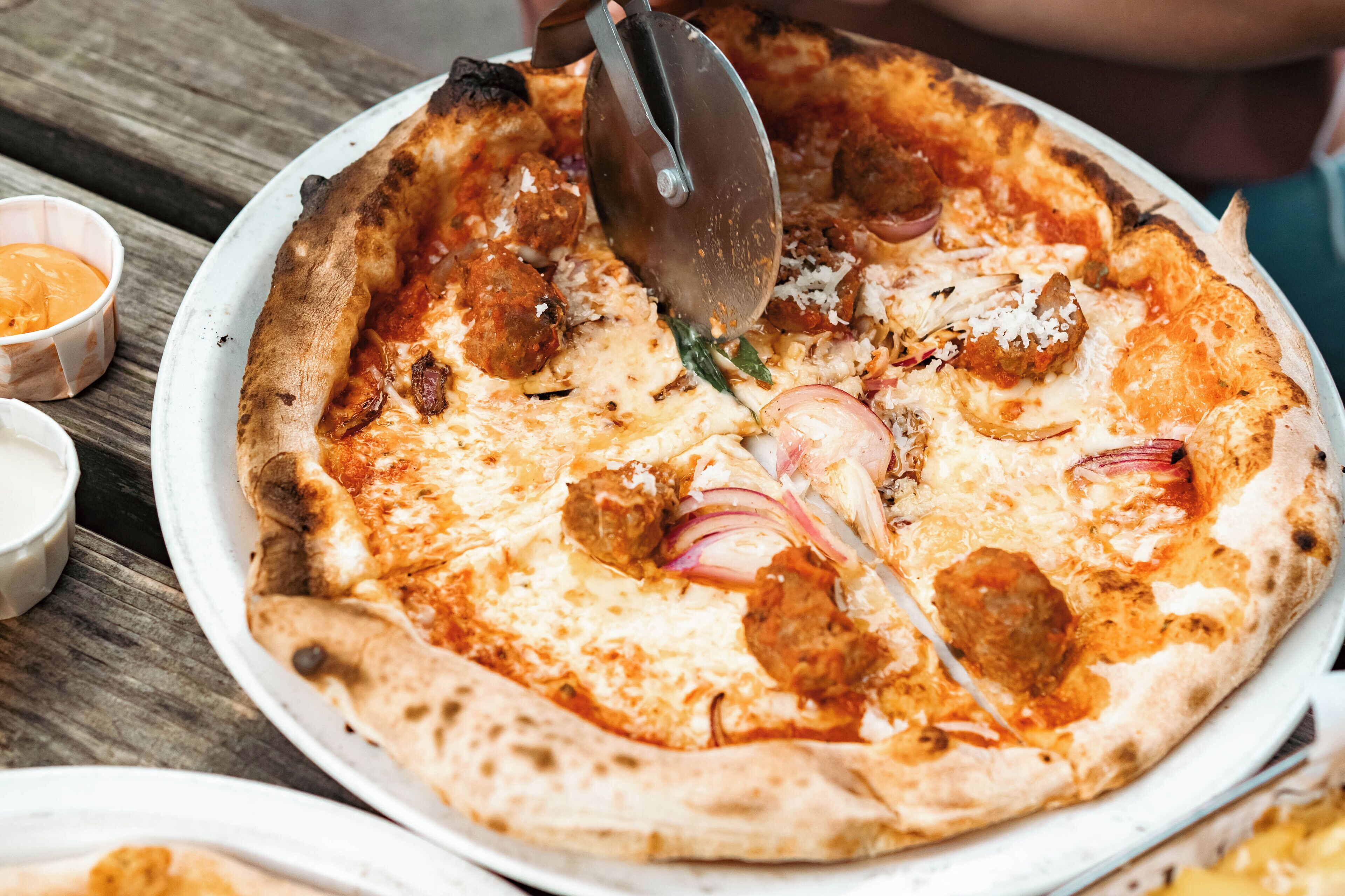 A pizza with toppings and a pizza cutter on a white plate.