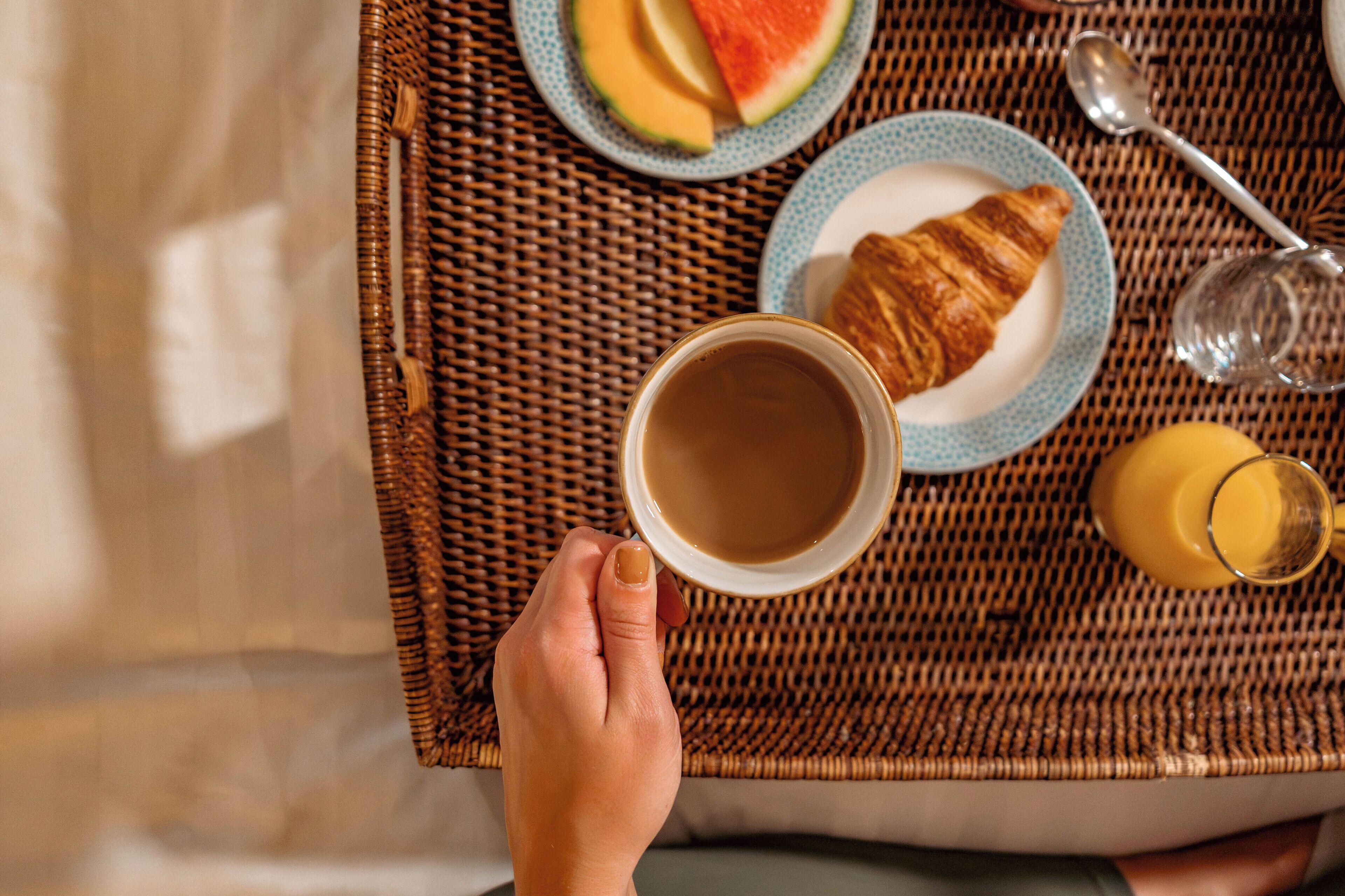 A tray with a croissant, a glass of juice, a cup of coffee, and a plate with a slice of watermelon.