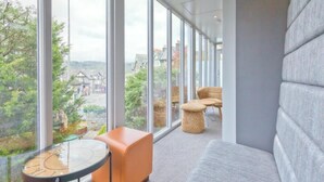 Een moderne kamer met grote ramen, een grijze bank, een ronde tafel en rieten stoelen.