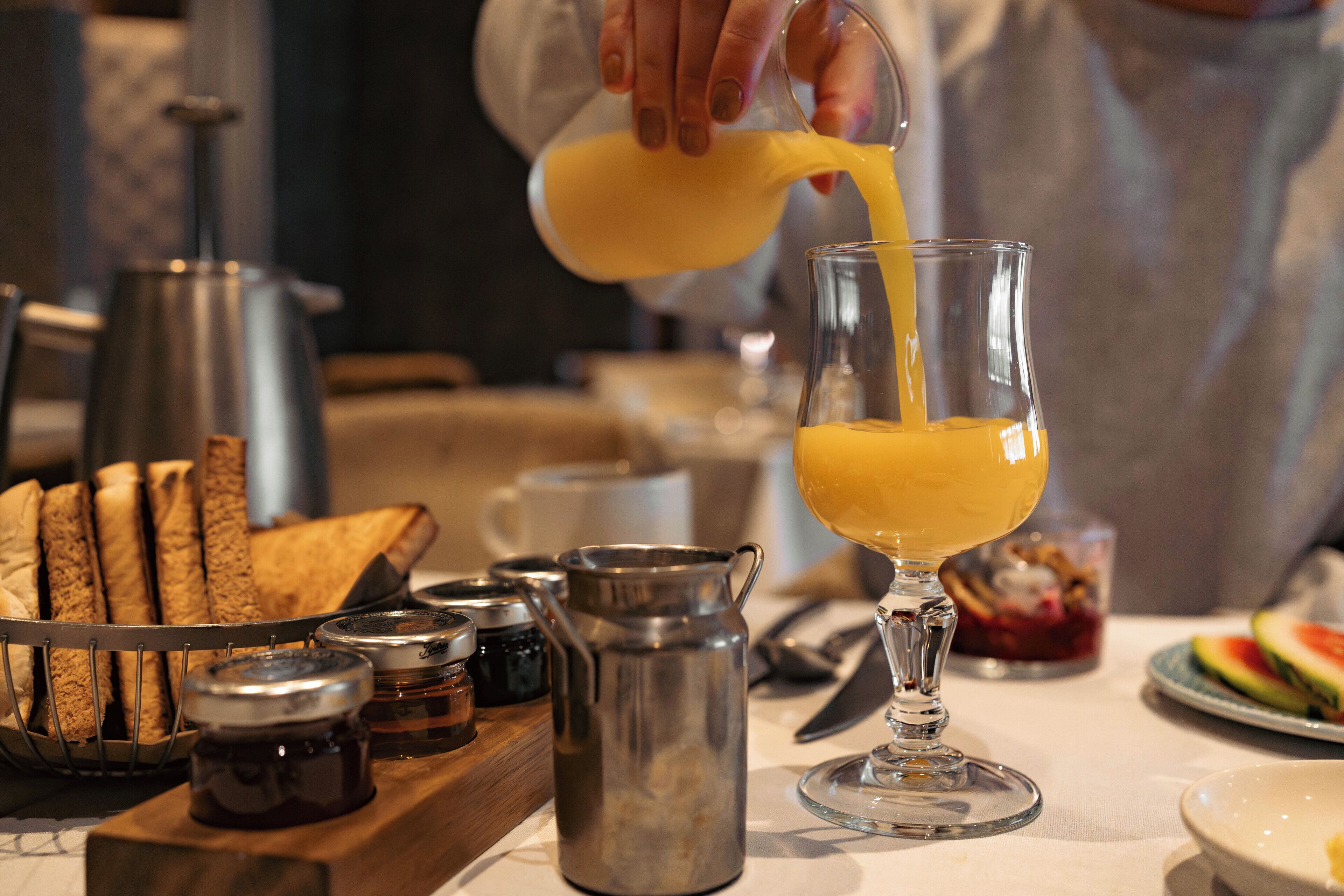 A breakfast setting with toast, jam, and a glass of orange juice being poured.