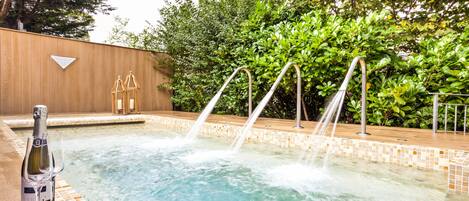 A hot tub with water jets, a bottle of champagne, and two glasses on a tiled ledge.