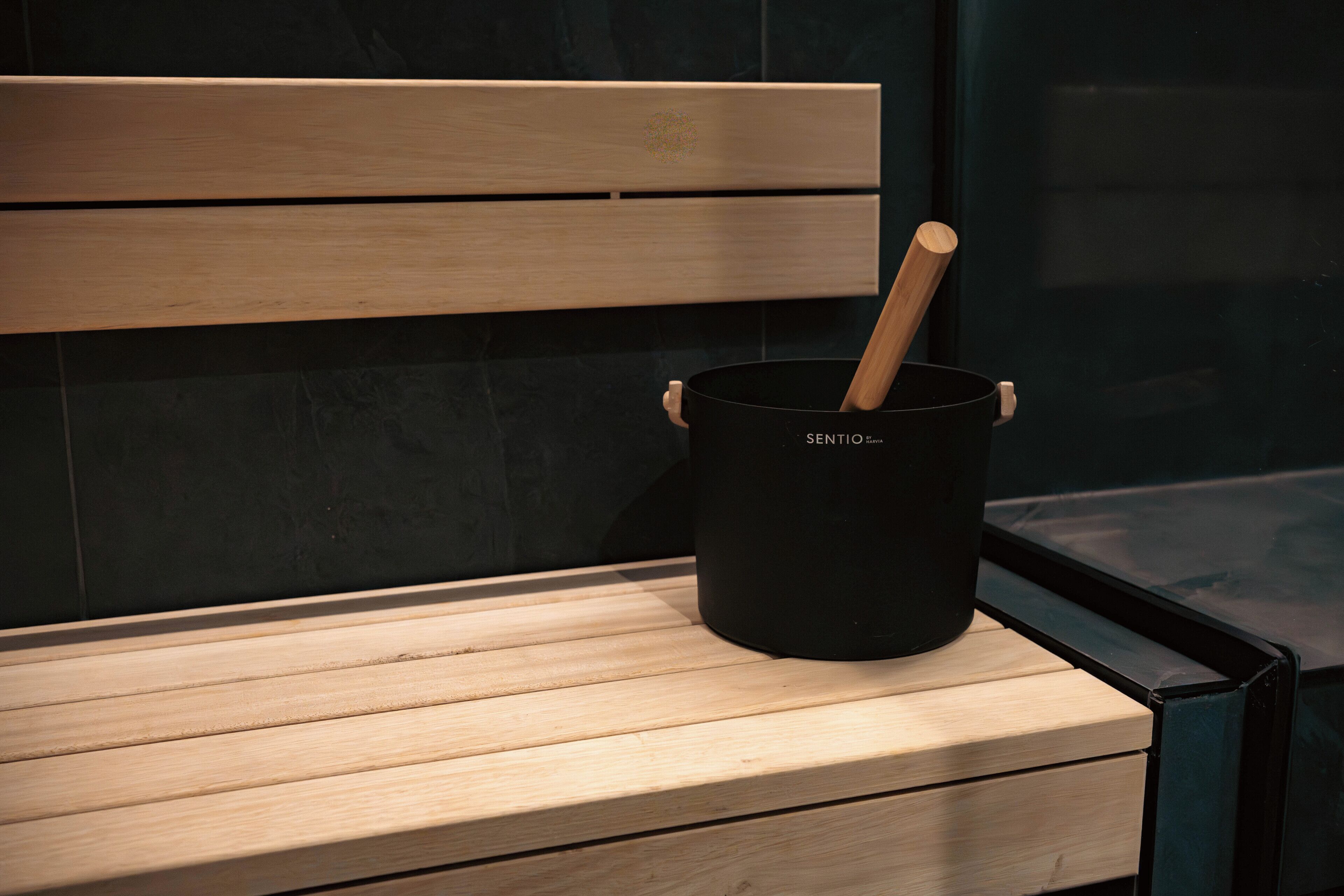 A wooden bench with a black pot labeled "SENTIO" and a wooden spoon inside it.