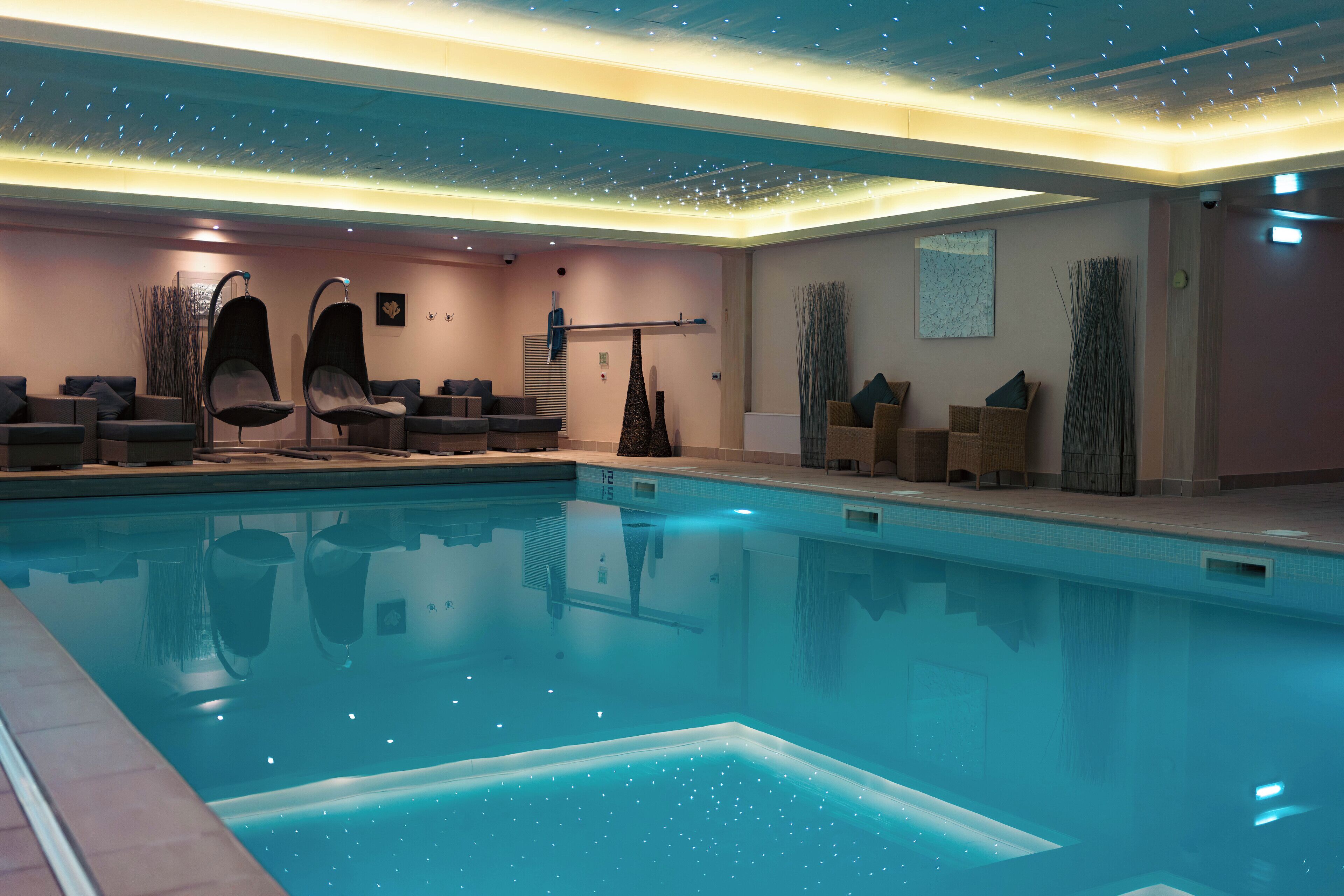 A modern indoor pool area with clear water, lounge chairs, and a ceiling with a starry light design.