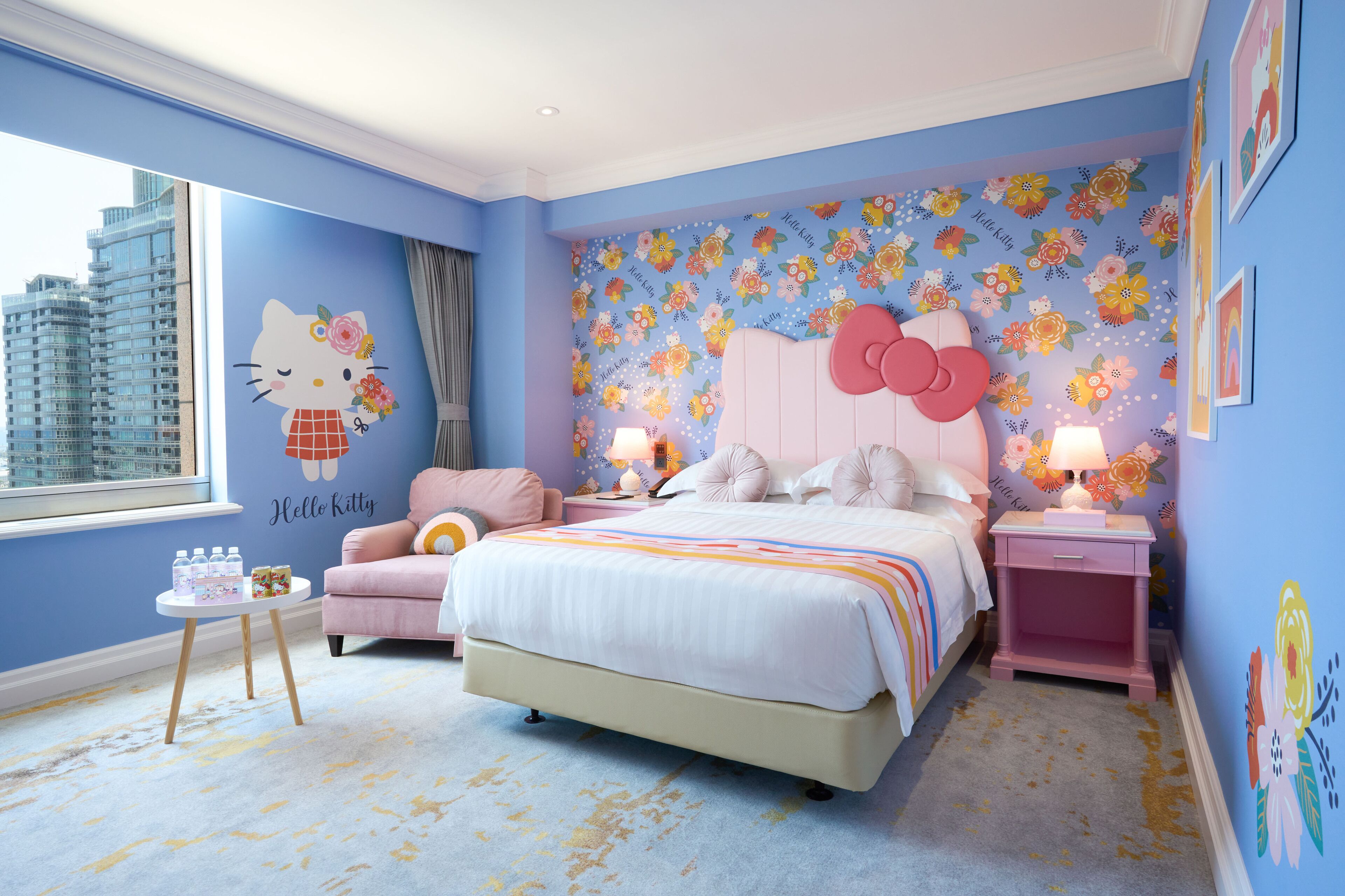 Ein Schlafzimmer mit floralem Wandbild, einem Hello Kitty Aufkleber, einem rosa Bett und Blick auf die Stadt.