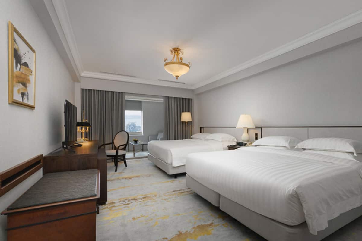 Ein Hotelzimmer mit zwei Betten, einem Schreibtisch, einem Stuhl und einem großen Fenster.