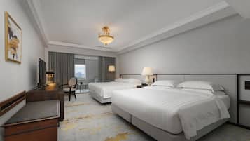 Ein Hotelzimmer mit zwei Betten, einem Schreibtisch, einem Stuhl und einem großen Fenster.