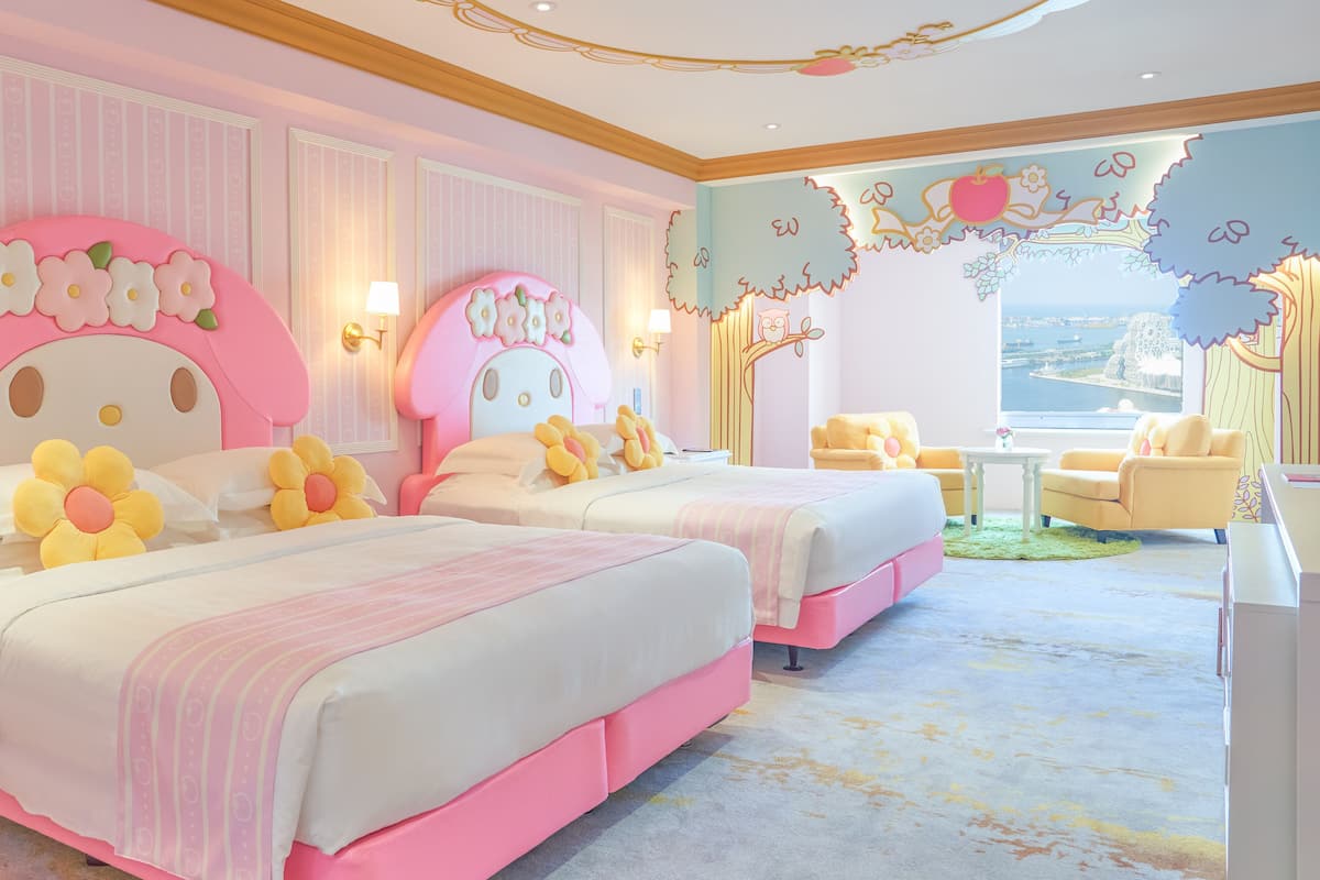 Ein zartrosa eingerichtetes Schlafzimmer mit zwei Betten, einem gelben Sessel und Meerblick.