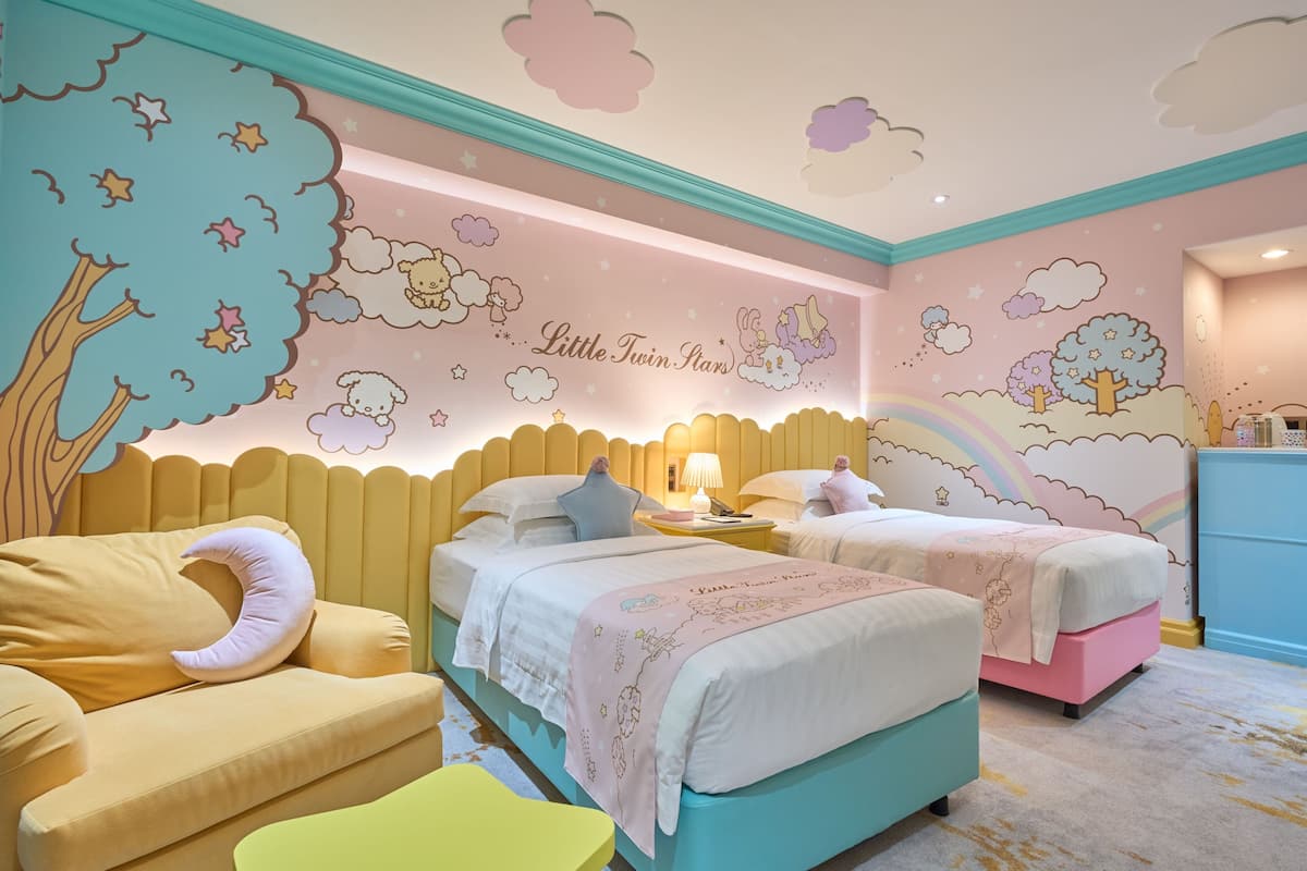 Ein Kinderzimmer mit zwei Betten, einer Schlafcouch und einer Kommode. An den Wänden befindet sich ein Wandbild mit Wolken, Sternen und Bäumen.
