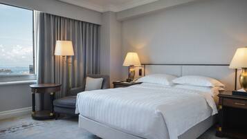A hotel room with a large bed, two bedside tables with lamps, a chair, and a view of the city through a window.