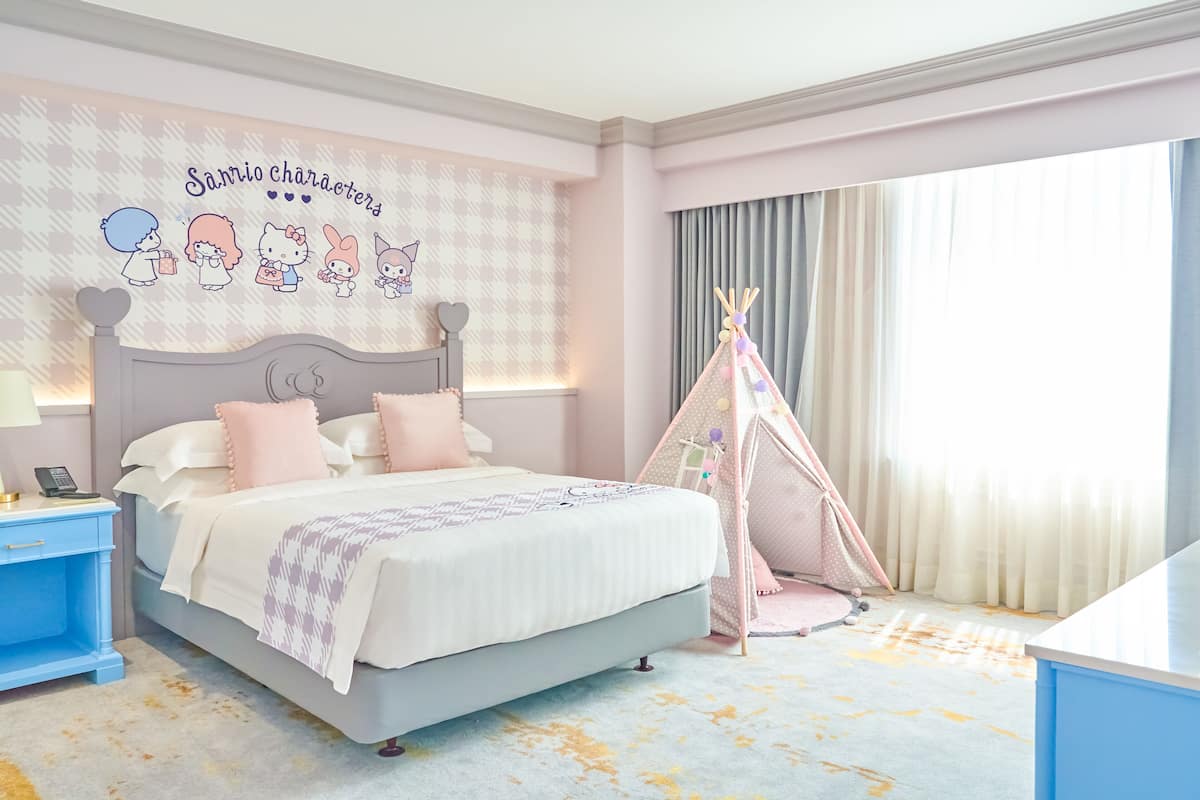 Ein Schlafzimmer mit Bett, Nachttisch, Wand mit Zeichentrickfiguren, Fenster mit Vorhängen und einem Teepee.